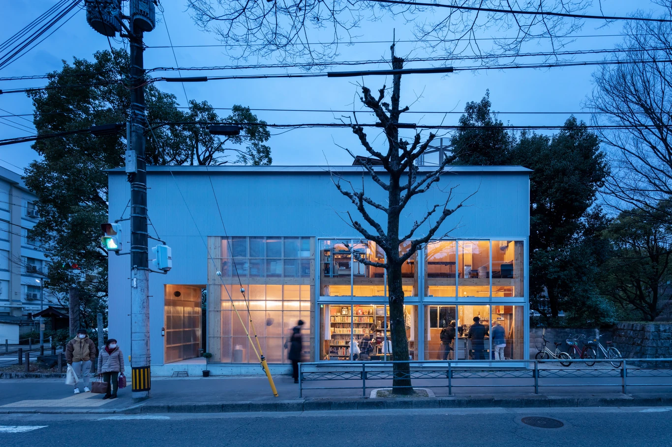 House S/Shop B (ba hütte) by KimuraMatsumoto Architects — Twilight photograph of a compact retail storefront with corrugated metal siding in cool grey, featuring two stacked rectangular window openings with minimal...