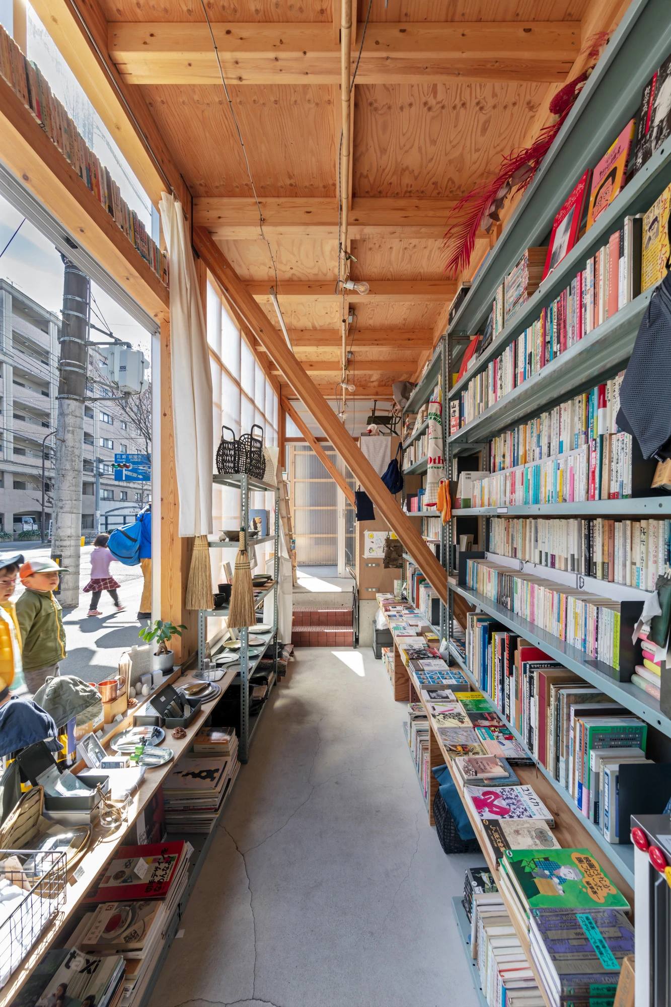 House S/Shop B (ba hütte) by KimuraMatsumoto Architects — Interior view of a narrow commercial space revealing exposed timber ceiling joists and plywood sheathing.