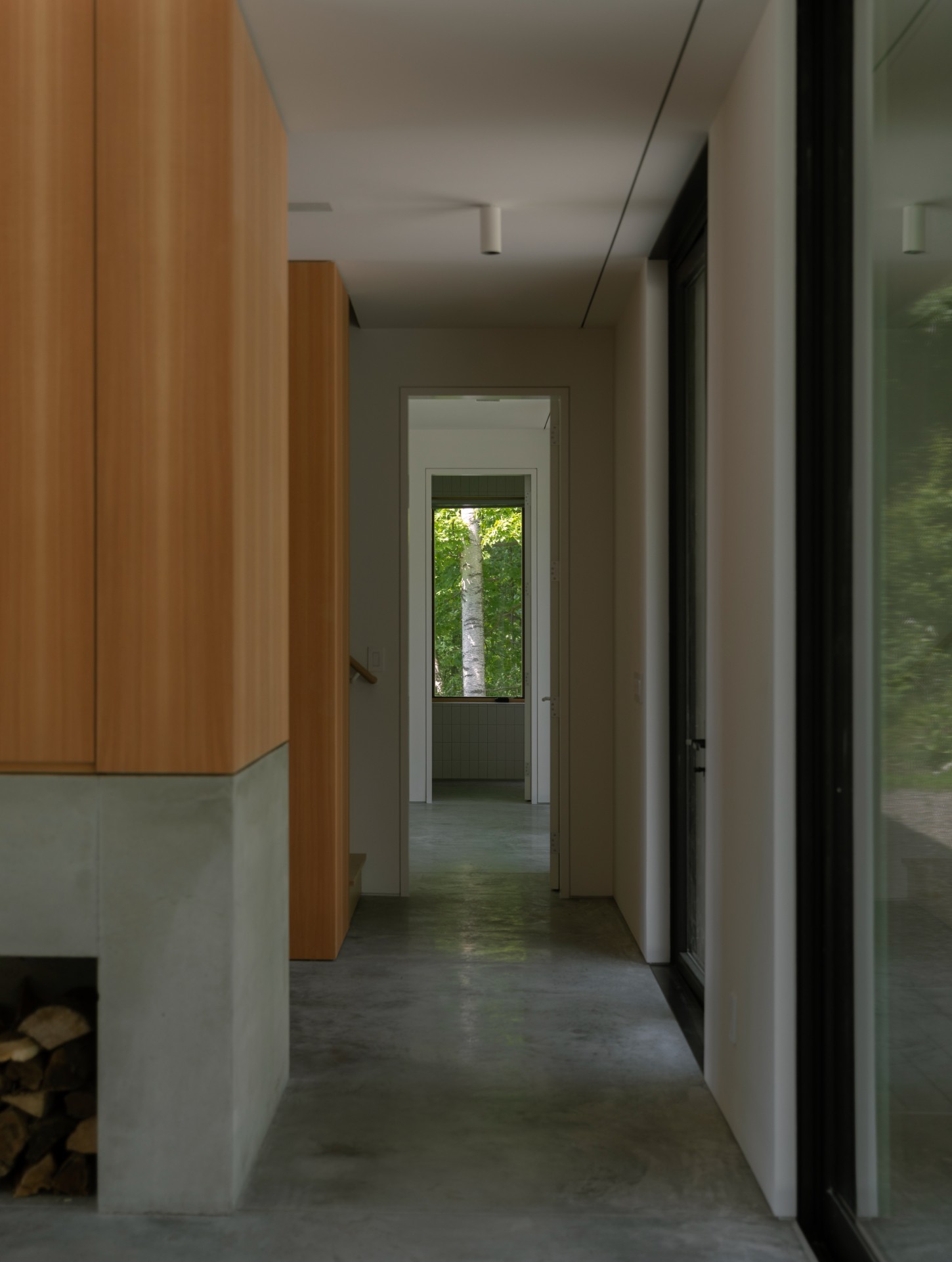 House in a Meadow by Group Projects Architecture — A linear corridor extends through the interior, framed by timber-clad walls in warm honey tones on the left and white plaster on the right.