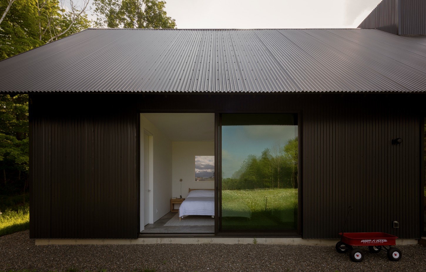 House in a Meadow by Group Projects Architecture — The guest house presents its primary façade to the meadow, a rectilinear form clad entirely in black corrugated metal whose linear ridges establish a...