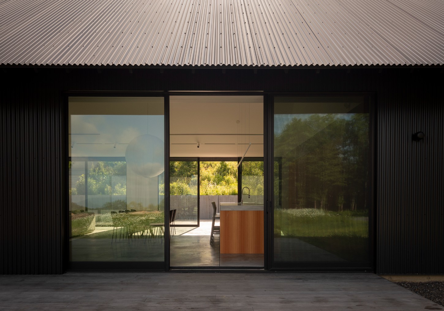 House in a Meadow by Group Projects Architecture — The corrugated metal facade dominates the view, its subtle wave texture creating horizontal striations across the black-clad wall.