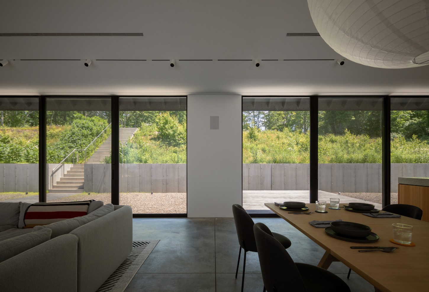 House in a Meadow by Group Projects Architecture — Interior view of the meadow-facing living and dining spaces, demonstrating the project's strategy of visual permeability.