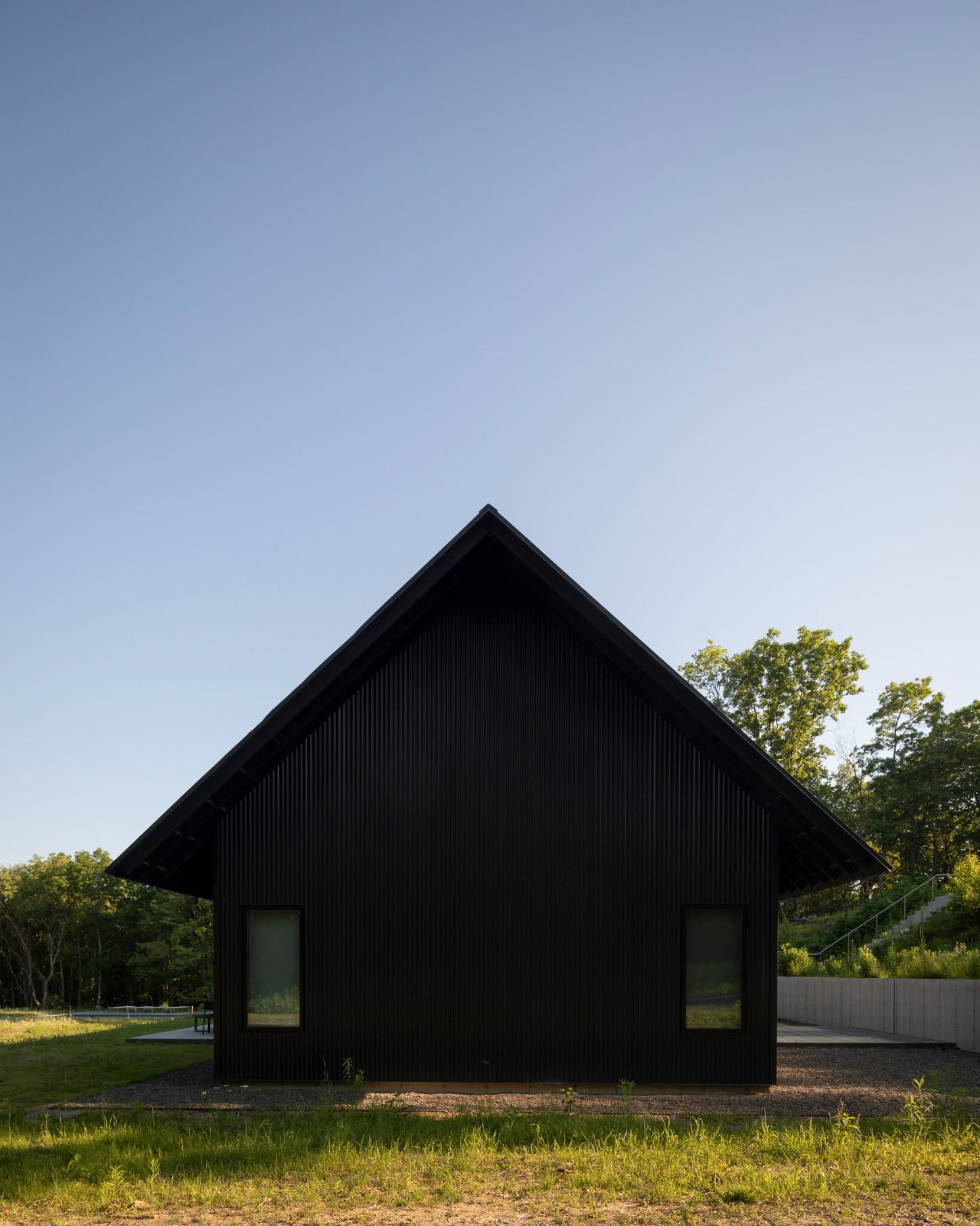 House in a Meadow by Group Projects Architecture — A black corrugated metal guest house occupies a meadow in Millerton, New York, its pitched-roof form silhouetted against clear sky.