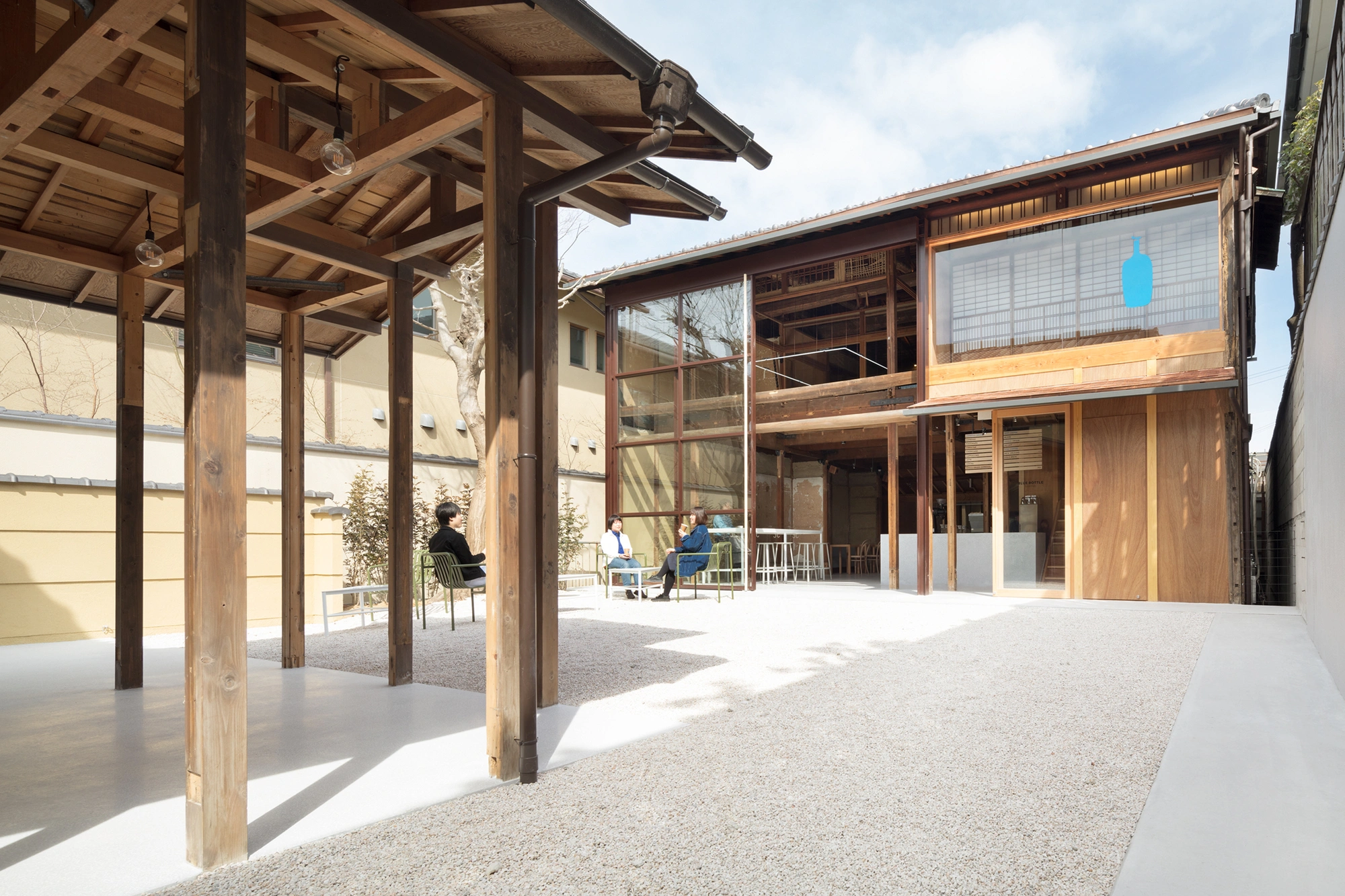 Blue Bottle Coffee Kyoto Cafe by Schemata Architects — The courtyard reveals the café's post-and-beam timber structure in full expression, with exposed latticed ceiling beams and coffered panels overhead...
