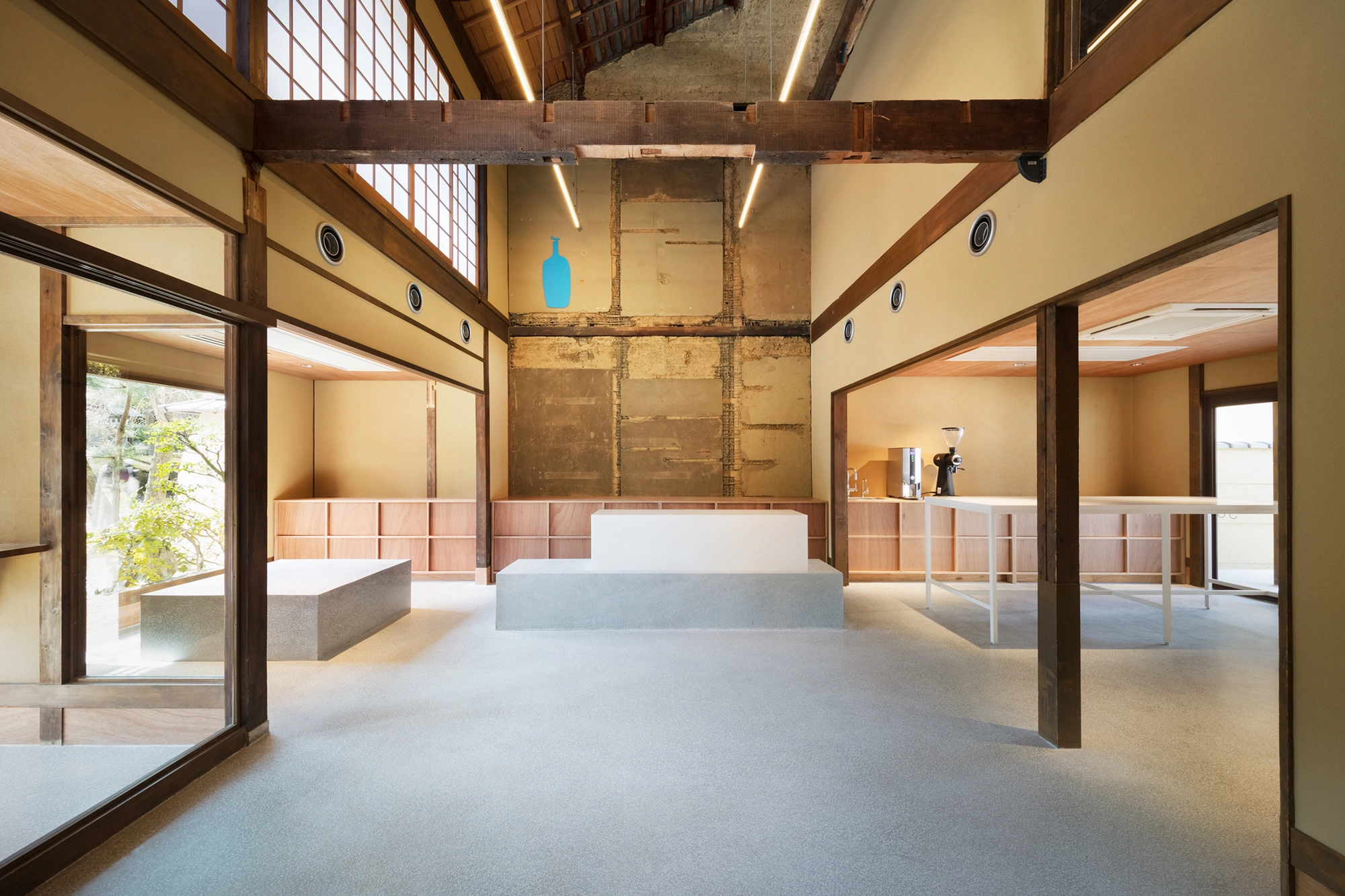 Blue Bottle Coffee Kyoto Cafe by Schemata Architects — The central hall of Blue Bottle Coffee Kyoto unfolds as a post-and-beam structure with exposed timber lattice overhead, filtered through linear fluorescent...