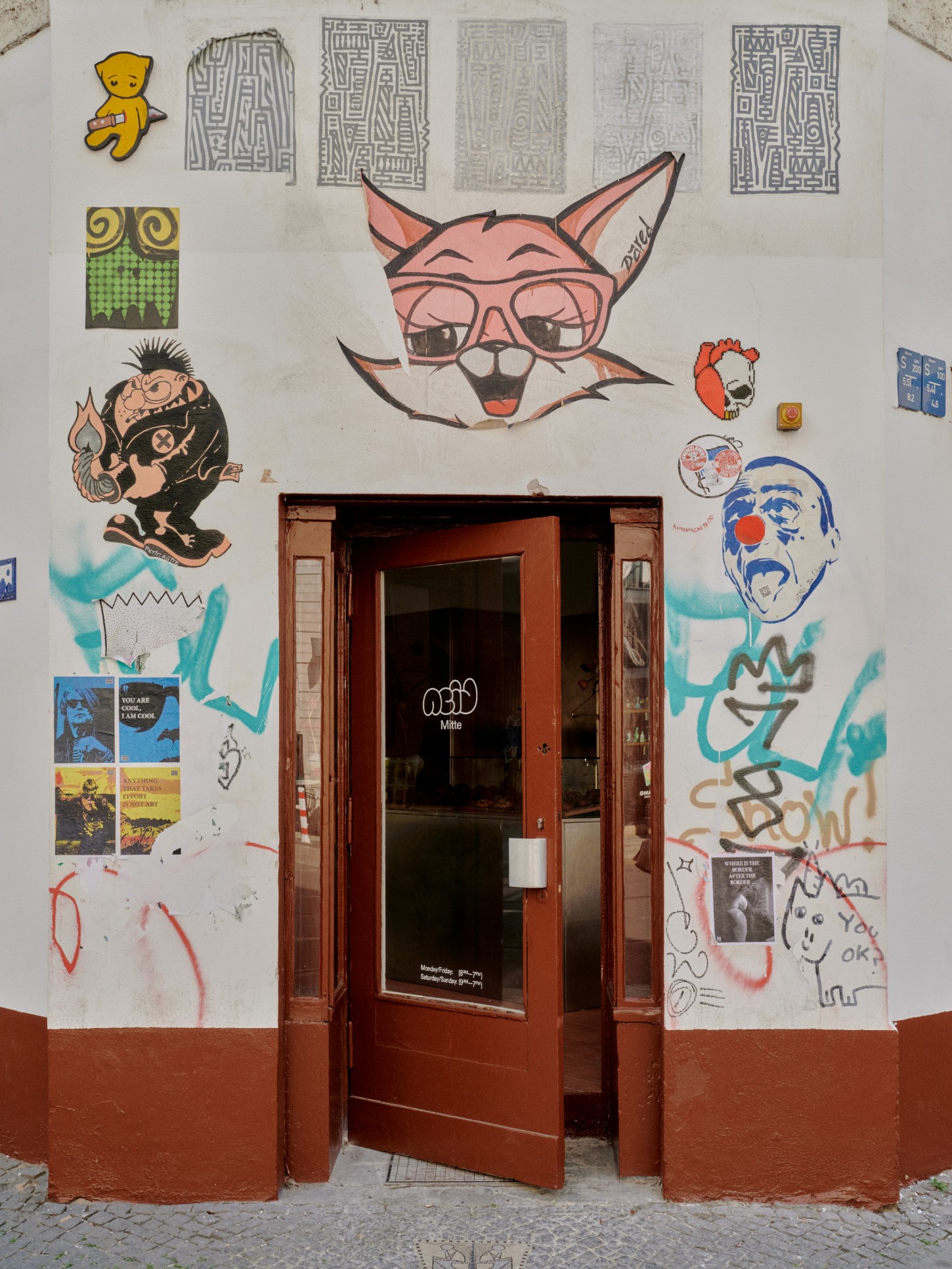 ACID Cafe by Plantea Studio by Plantea Estudio — The street-facing entrance to ACID Cafe features a terra-cotta-rendered lower wall and white plaster upper surface serving as a canvas for layered graphic...