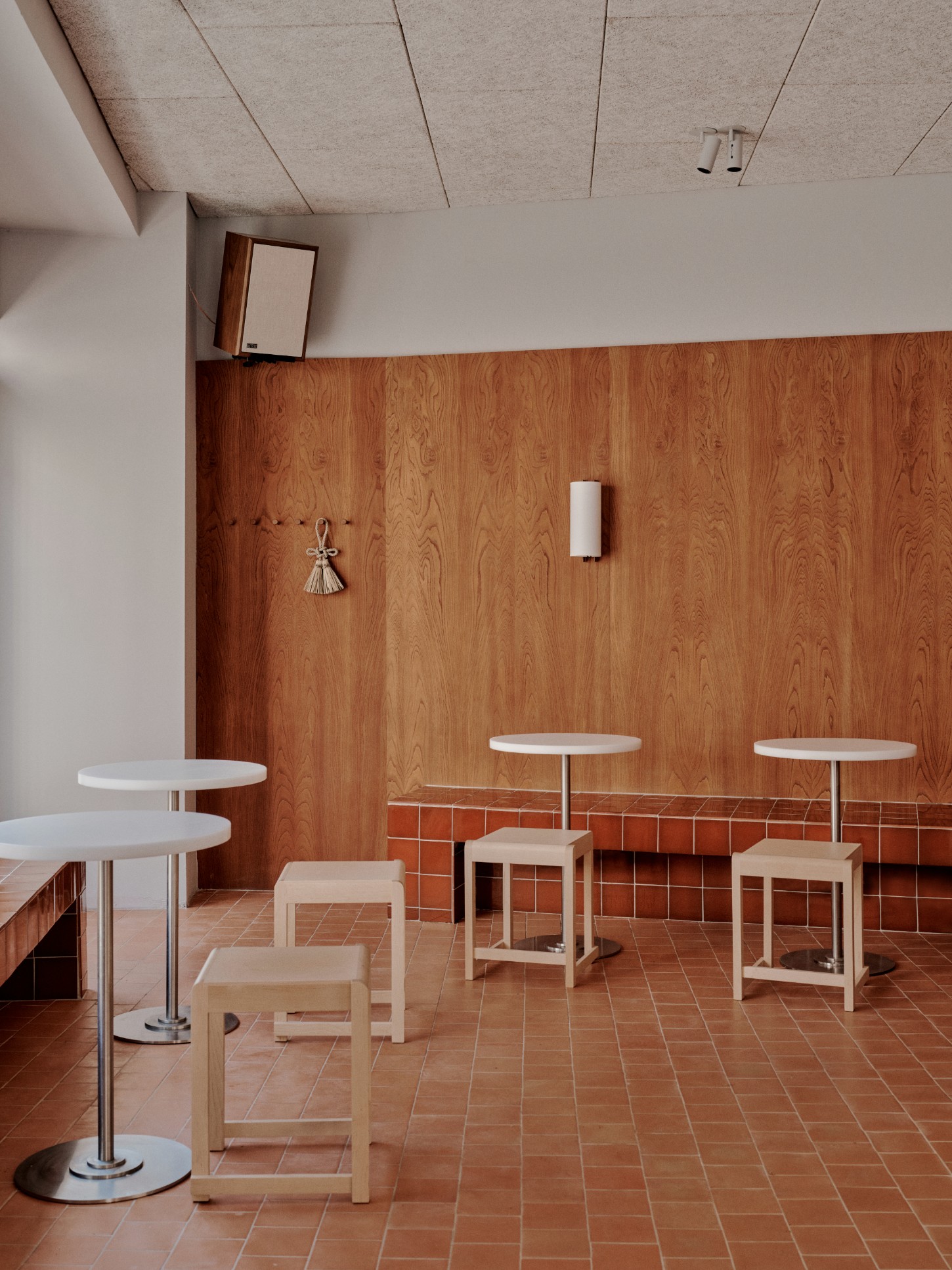 ACID Cafe by Plantea Studio by Plantea Estudio — ACID Cafe's dining area showcases a restrained material palette anchored by a herringbone-pattern terracotta brick floor in warm rust tones.
