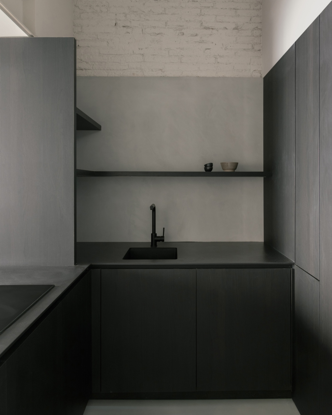 Casa Norte by CORREA Studio — A compact kitchen alcove defined by dark charcoal cabinetry with vertical panel divisions and recessed handles, anchoring the lower half of the composition.