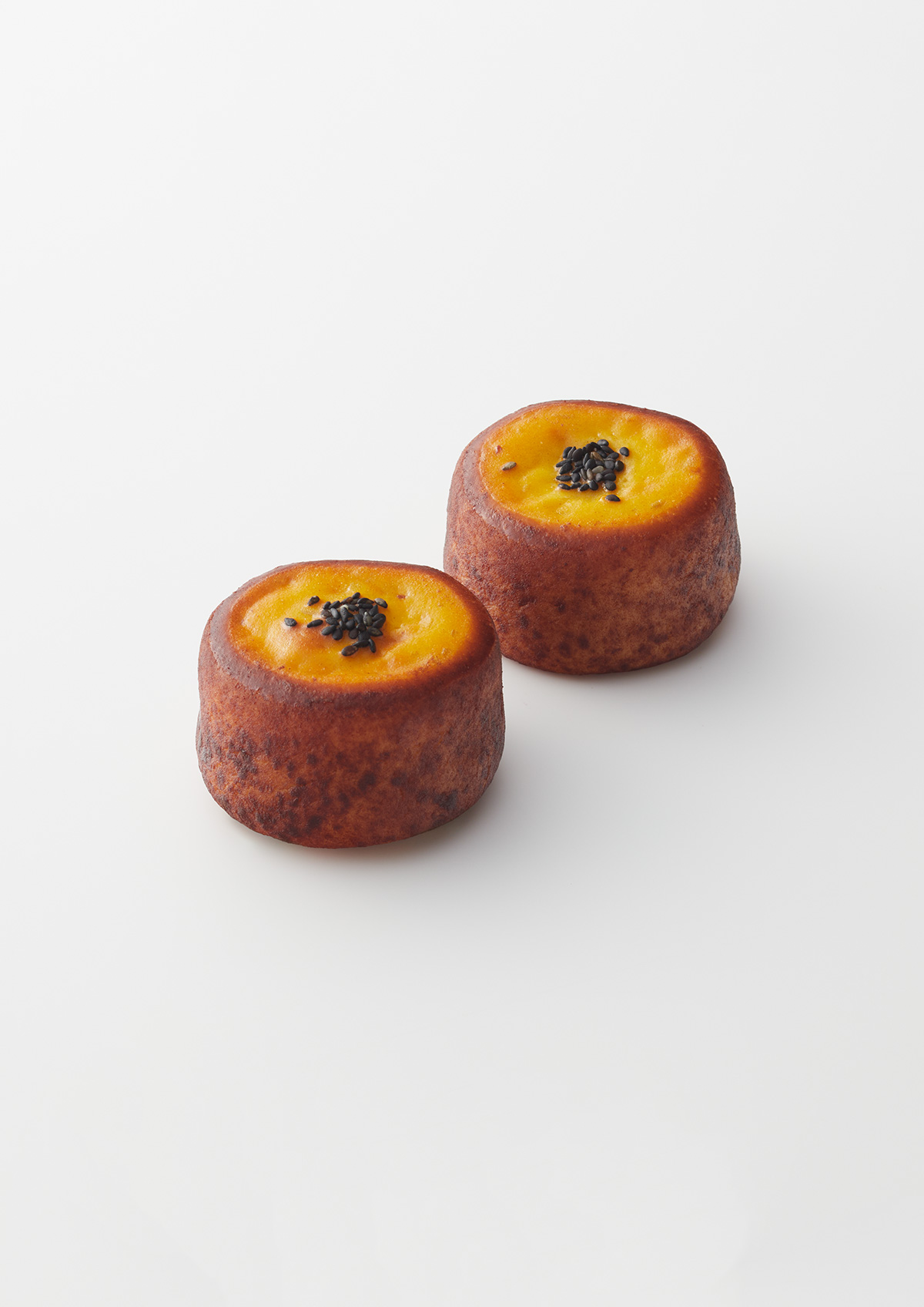 La Collina Ōmi-Hachiman by Terunobu Fujimori + Michele De Lucchi — Two cylindrical pastries with caramelized brown exterior surfaces and golden-yellow tops, each crowned with a dark cluster of what appears to be black...