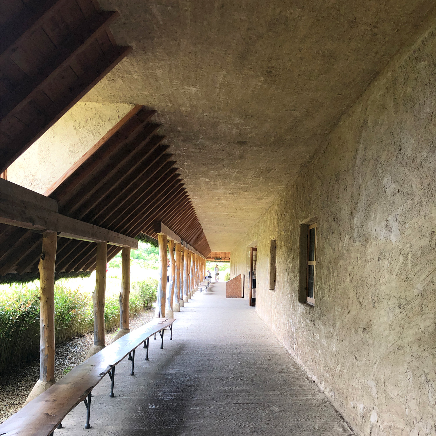 La Collina Ōmi-Hachiman by Terunobu Fujimori + Michele De Lucchi — A covered passage extends beneath a concrete soffit with exposed timber beam structure, revealing the rhythmic repetition of wooden posts supporting the...