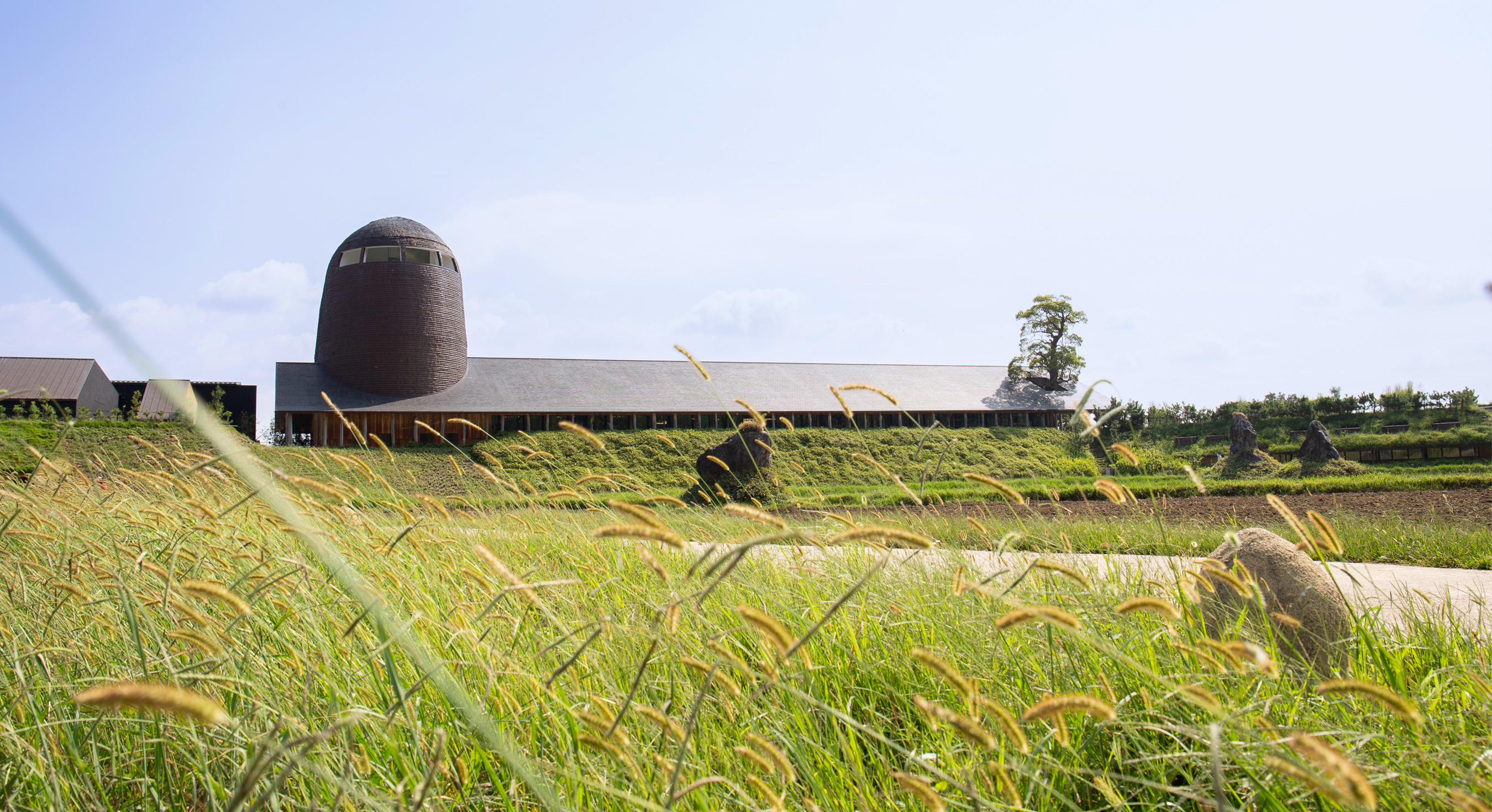 La Collina Ōmi-Hachiman by Terunobu Fujimori + Michele De Lucchi — The flagstone-roofed structure anchors a cultivated hillside landscape in Omihachiman.