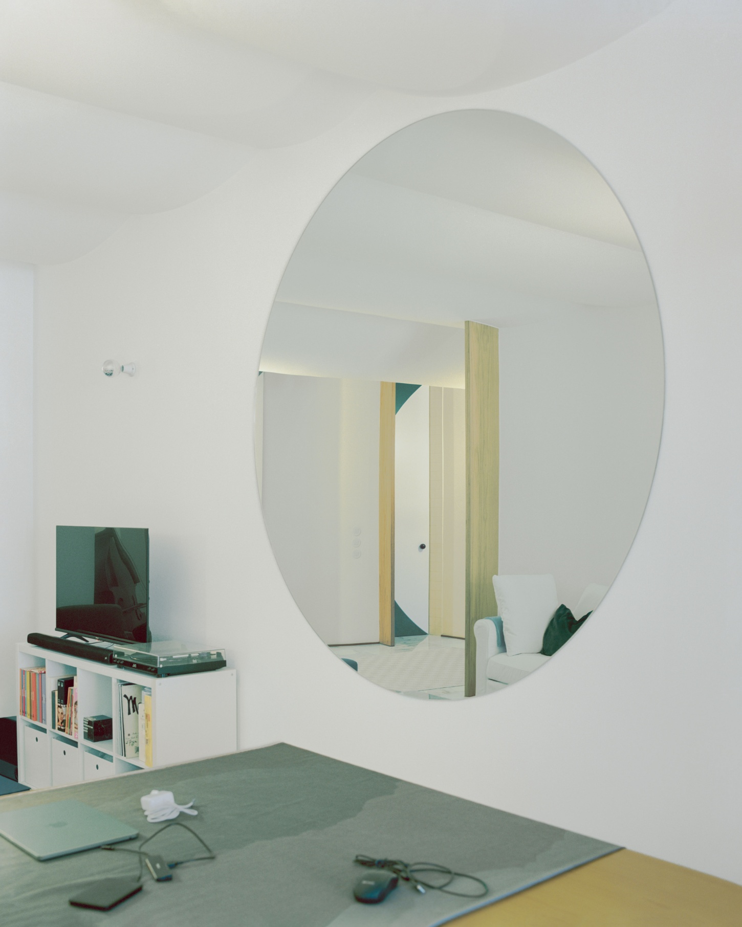'Fireworks in White' by Willem Pab — A workspace defined by a large oval mirror mounted on white plaster wall, reflecting the interior's geometric and material divisions.