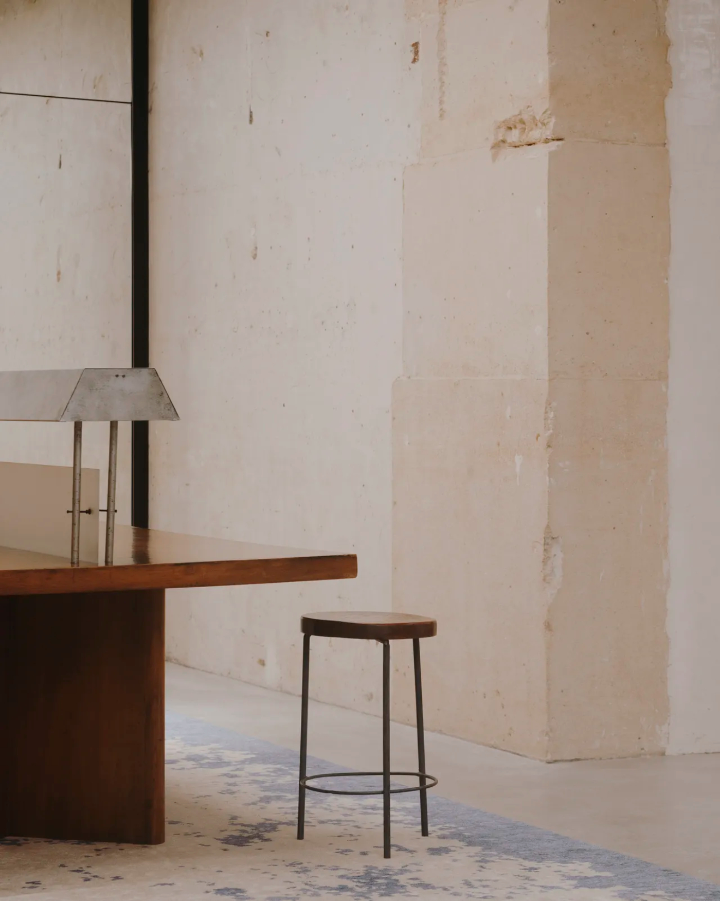 Saint Laurent Babylone in Paris — A curved walnut table anchors the foreground, its organic form contrasting sharply with the angular metal bar stool positioned before it.