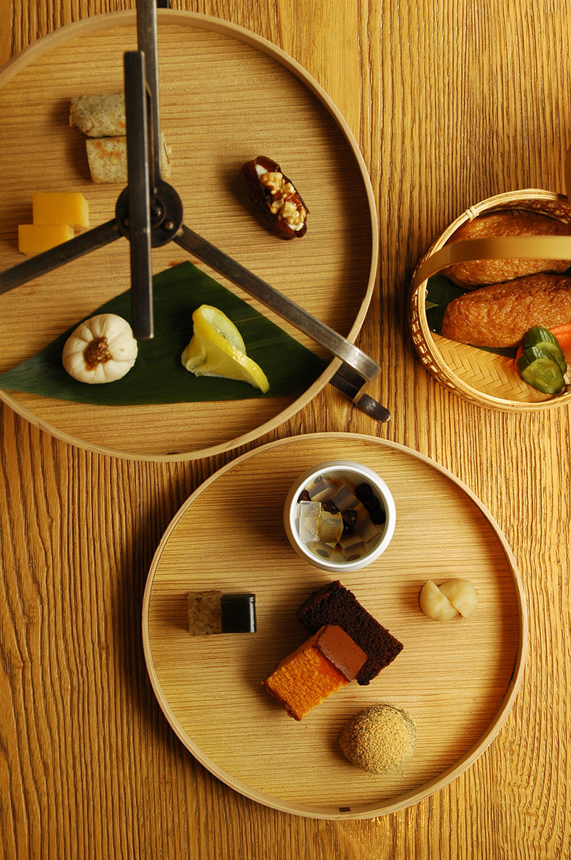 HIGASHIYA man marunouchi Tokyo — Overhead view of wooden circular serving trays arranged on a timber surface, each displaying carefully curated food items and tableware samples.