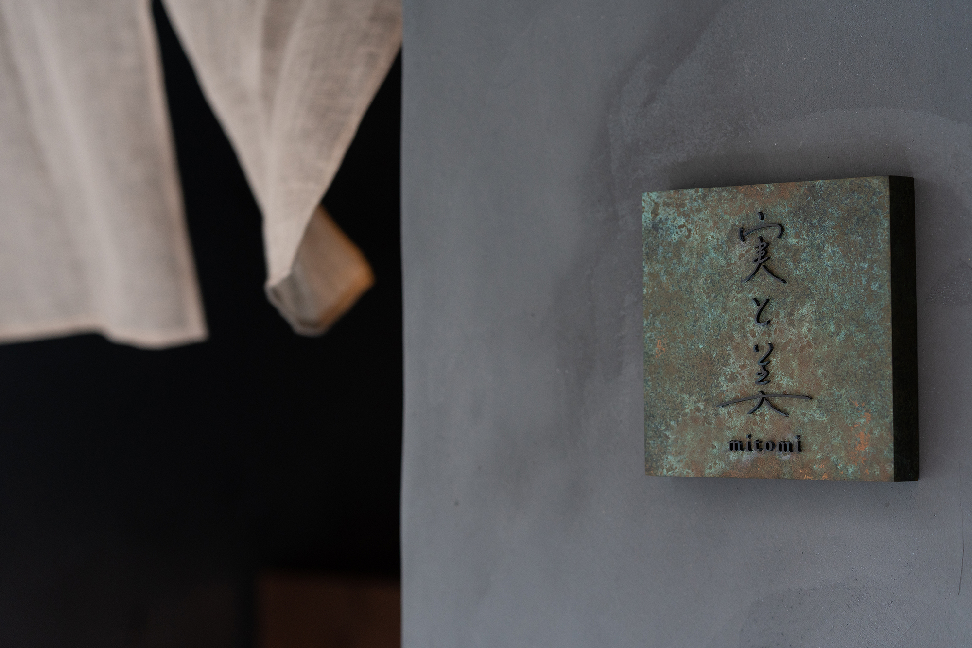 mitomi by Koyori + Aterier Salt — A close-up view of the mitomi storefront focusing on a patinated copper-faced product box positioned against a rendered gray wall.
