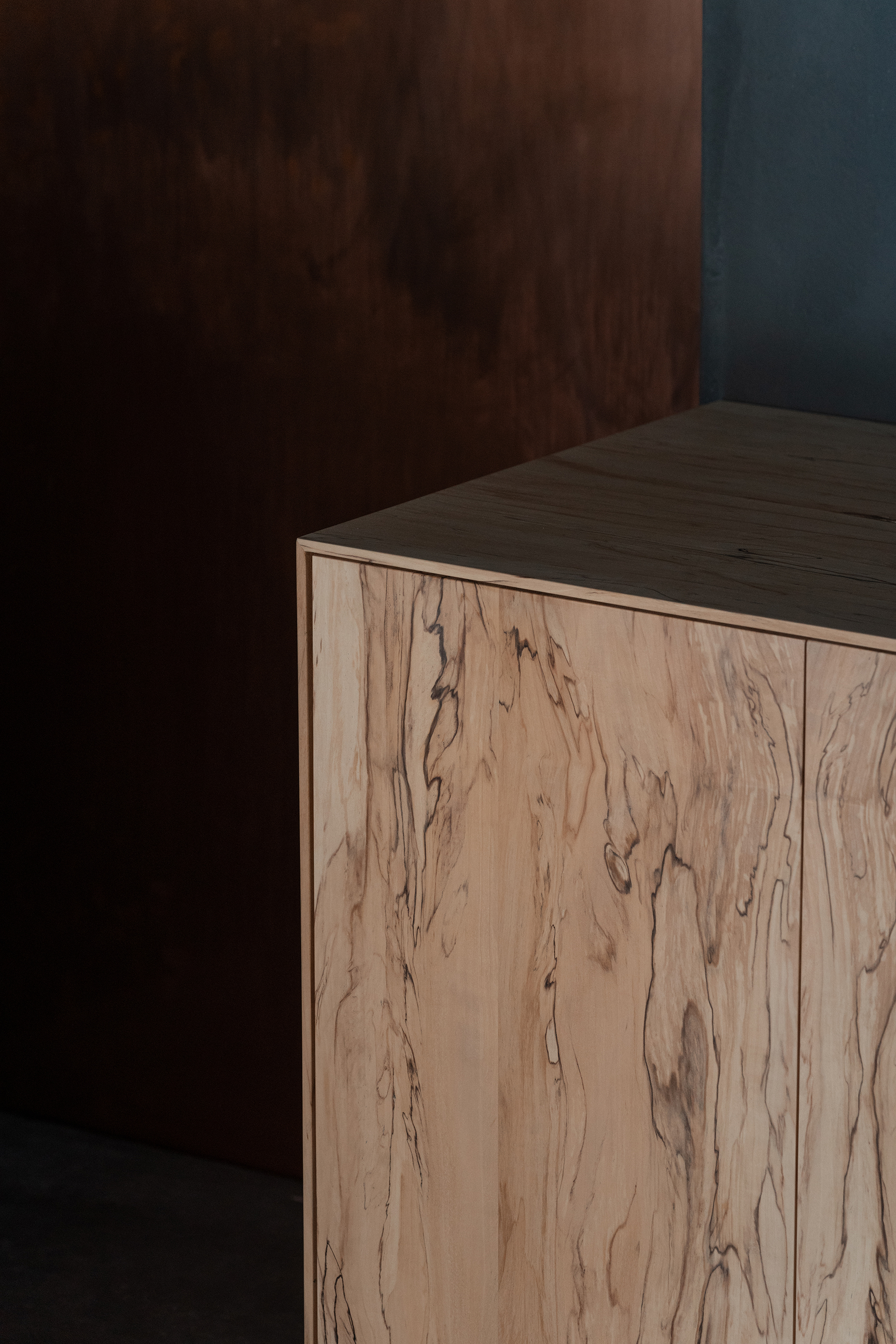 mitomi by Koyori + Aterier Salt — A light-rendered wooden cabinet with visible grain patterns and dark knots sits isolated in a darkened interior, its pale surface illuminated to create...