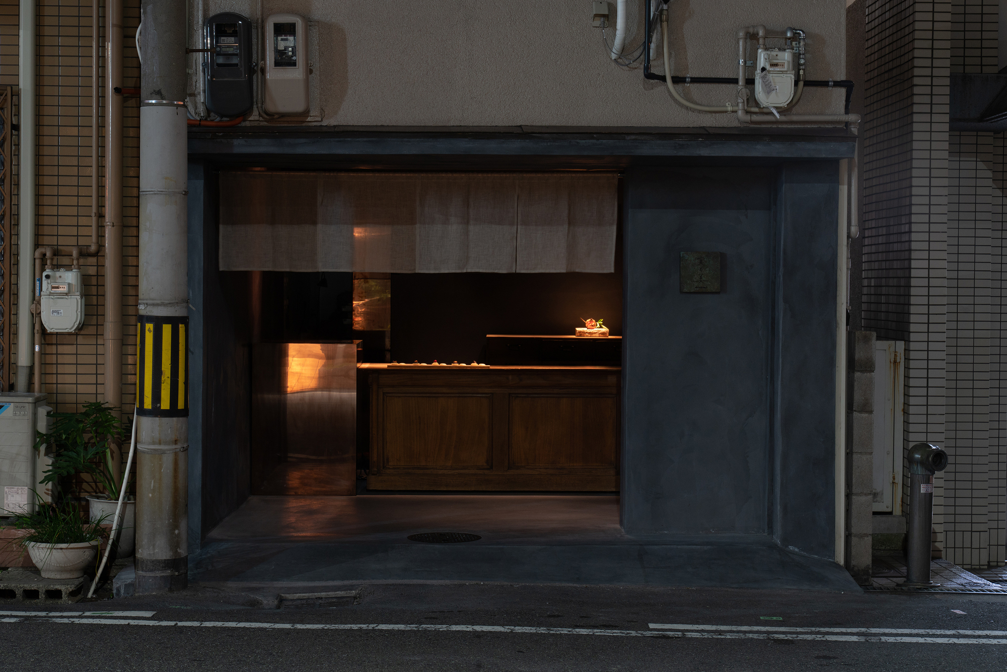 mitomi by Koyori + Aterier Salt — Evening photograph of a storefront entrance with black-rendered walls and ceiling creating a recessed passage.