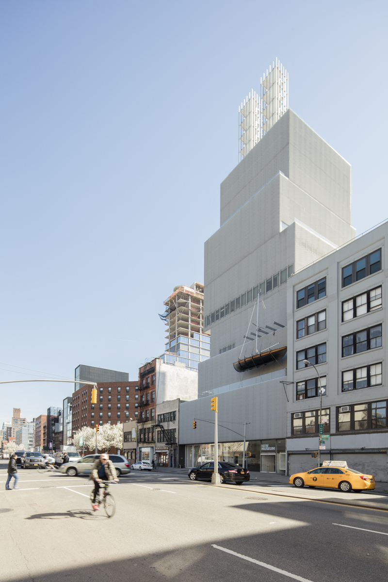 New Art Museum by SANAA — Street-level perspective of SANAA's stacked rectangular volumes reveals the sharp materiality of the white rendered facade rising above surrounding brick...