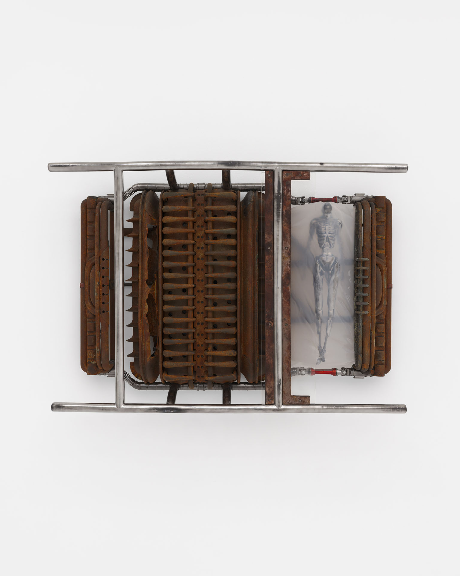 ENDO– by Taylor Ashby Hawkins at ASHES/ASHES — A symmetrical assemblage mounted on a white wall presents disassembled automotive engine components—ribbed cylinder heads and finned structures in oxidized...