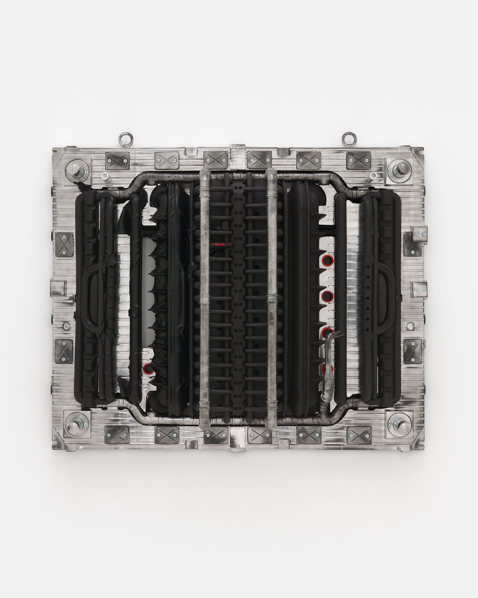 ENDO– by Taylor Ashby Hawkins at ASHES/ASHES — A wall-mounted sculptural assembly presents disassembled automotive engine components—ribbed aluminum cylinder heads and finned cooling structures—arranged...