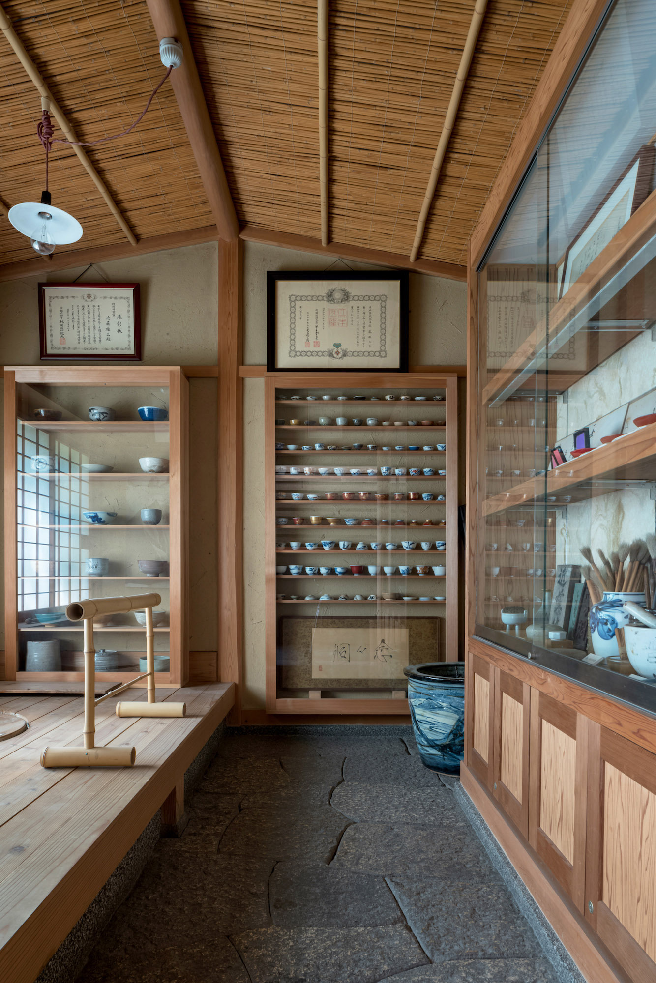 Kondo Museum in Kyoto by Mamiya Shinichi Design Studio — Interior view of the museum's display corridor featuring floor-to-ceiling glass-fronted cabinetry with horizontal timber shelving displaying blue-and-white...