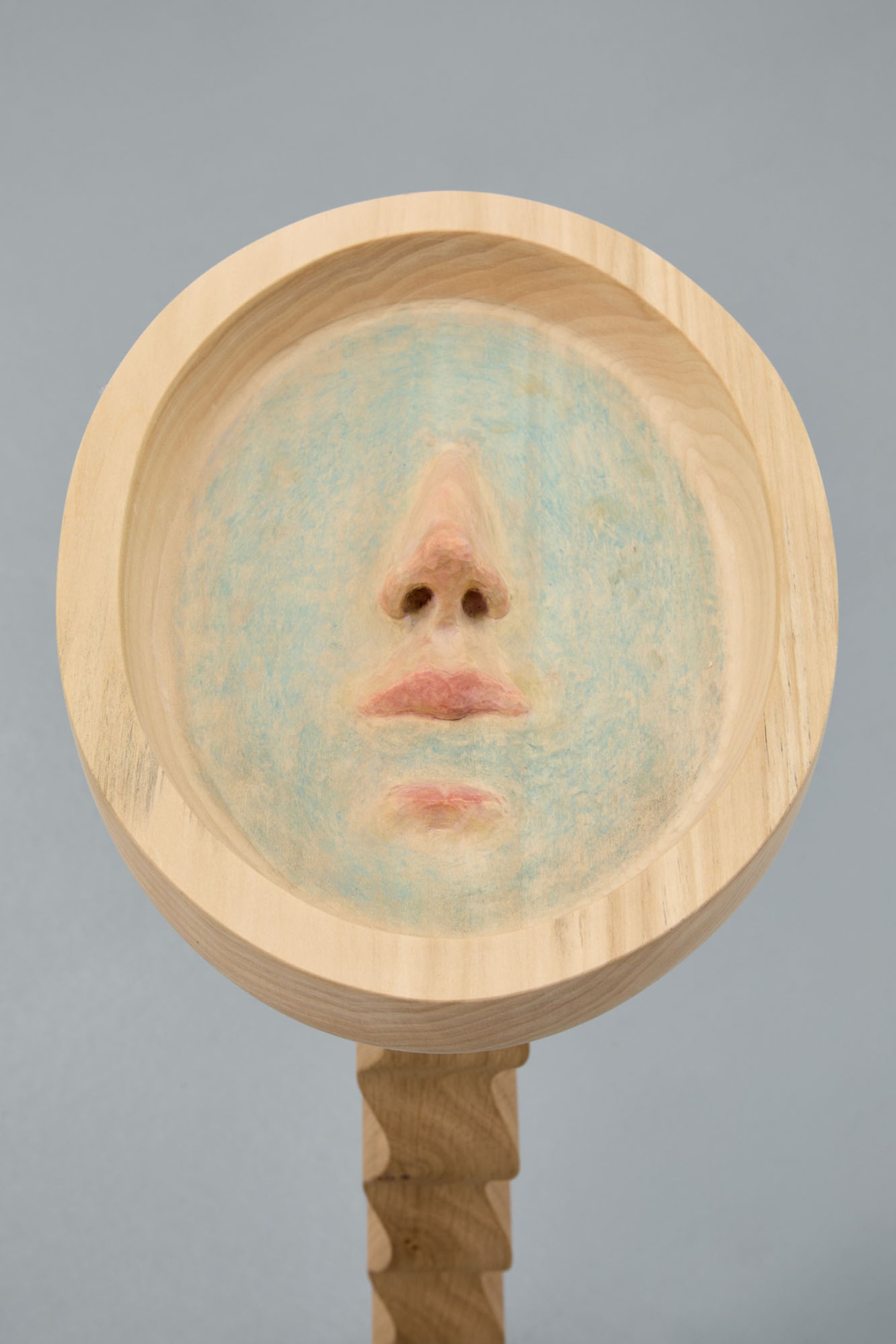 Thirst by Eliška Konečná at Polansky — Konečná's hand-held wooden mirror presents a singular face emerging from pale timber, its surface carved in relief.
