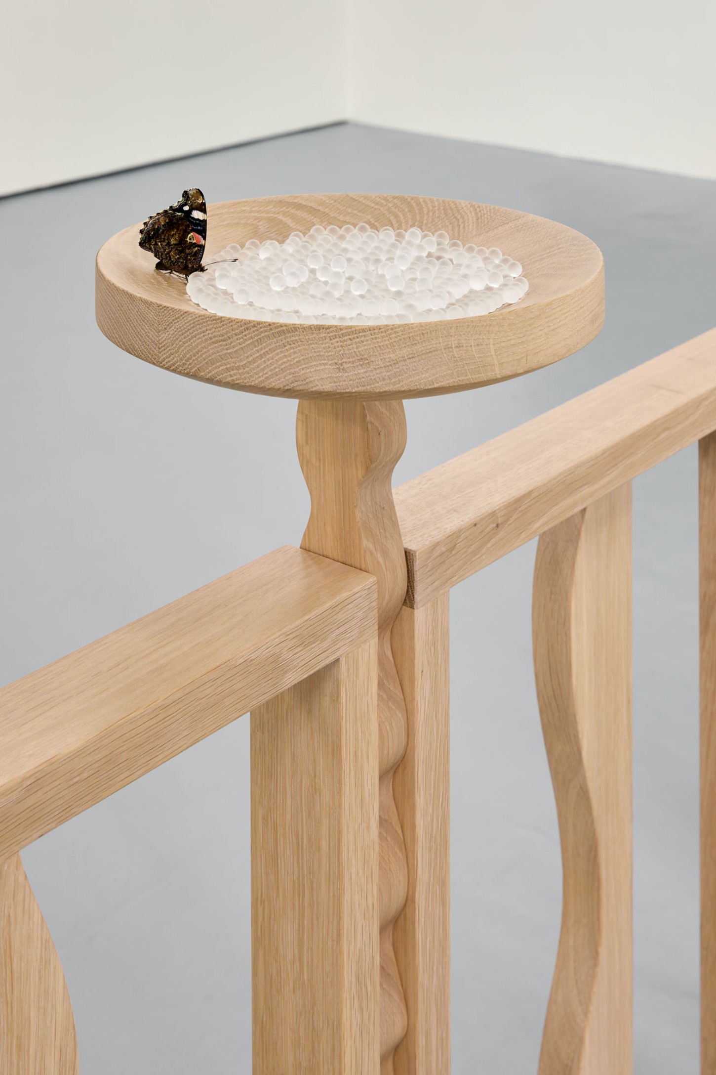 Thirst by Eliška Konečná at Polansky — A wooden pedestal table crafted from light oak holds a shallow circular bowl filled with white spherical forms—likely salt crystals or similar granular...