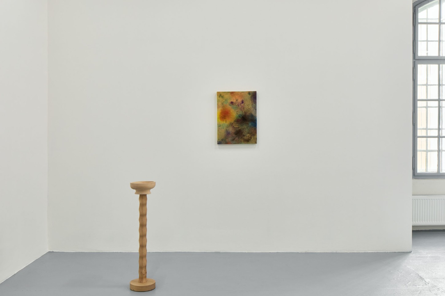 Thirst by Eliška Konečná at Polansky — A wooden pedestal with turned detailing stands isolated on a gray concrete floor within a white gallery space.