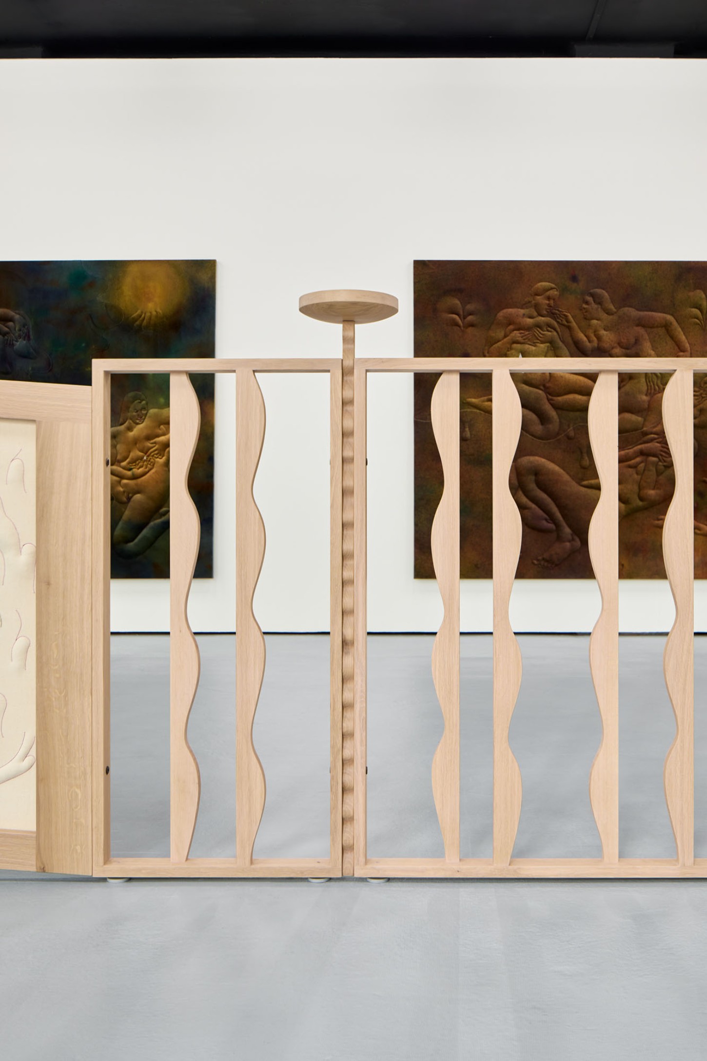 Thirst by Eliška Konečná at Polansky — Light timber display cases with sinuous curved mullions frame relief carvings depicting intertwined nude figures in classical poses.
