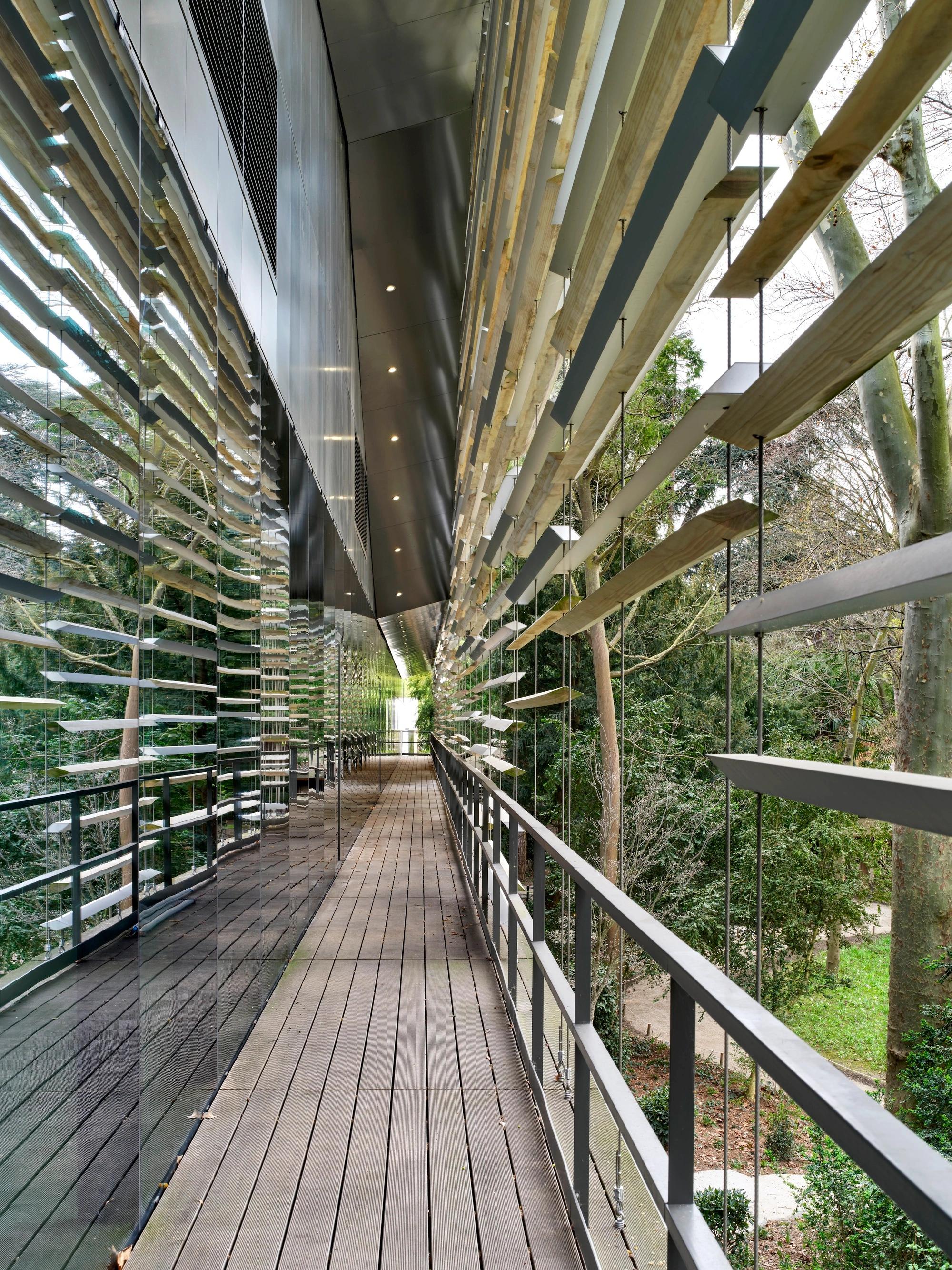 Albert Kahn Museum by Kengo Kuma & Associates — A linear passage framed by continuous horizontal aluminum striations on the left facade, with exposed timber beams spanning overhead at regular intervals.