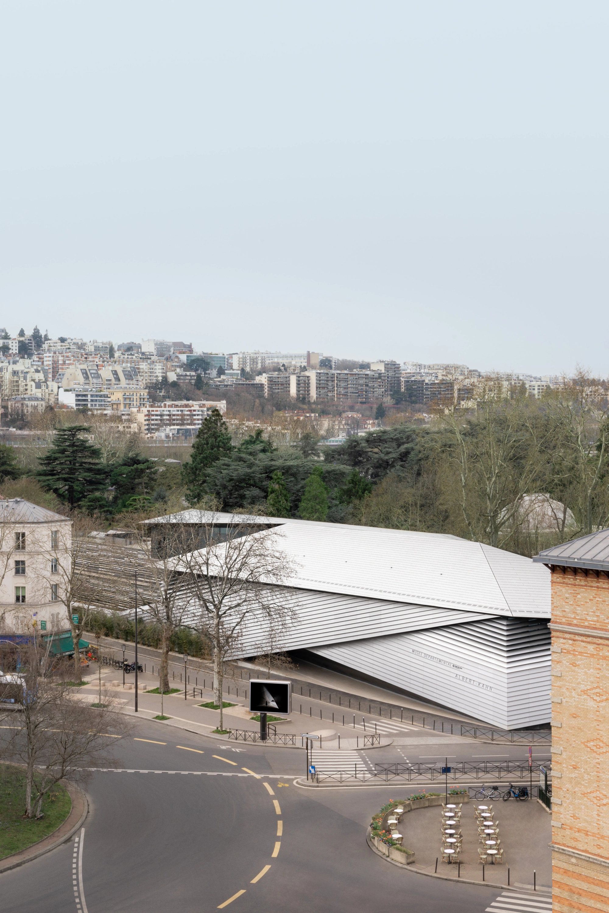Albert Kahn Museum by Kengo Kuma & Associates — The Albert Kahn Museum's undulating aluminum-clad form dominates the foreground, its continuous horizontal striations catching afternoon light across the...