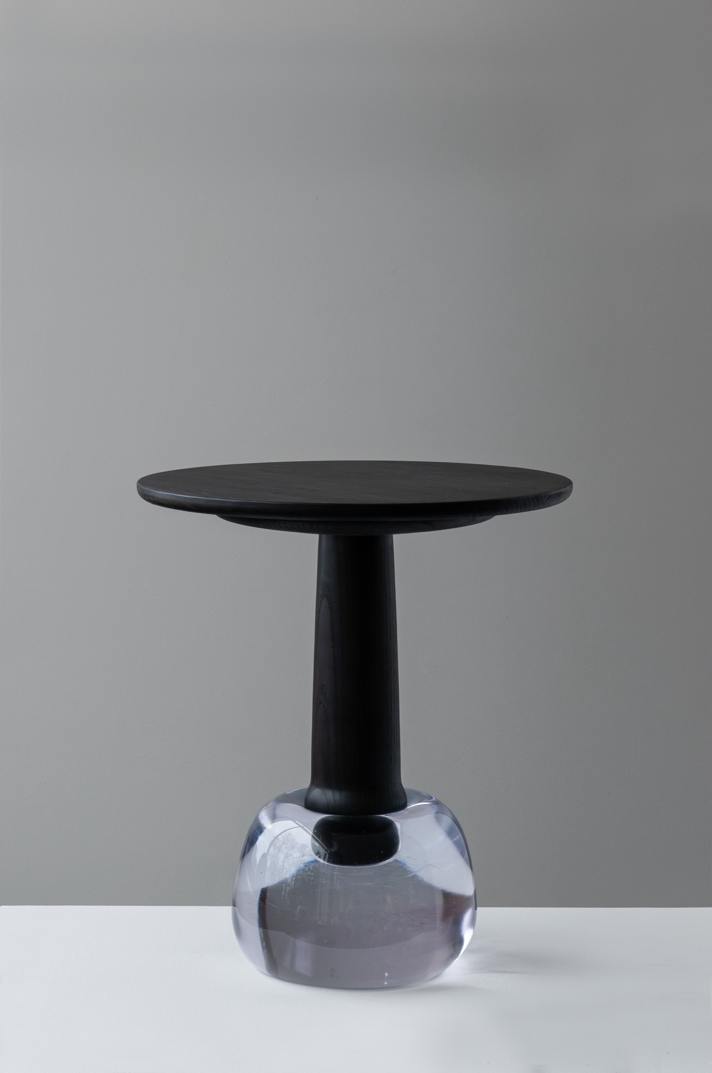 'Burn & Turn' by Adrian Bursell + Siri Svedborg — A pedestal table from 'Burn & Turn' pairs a turned timber column with vertical fluting against a hand-cast glass base in pale periwinkle.
