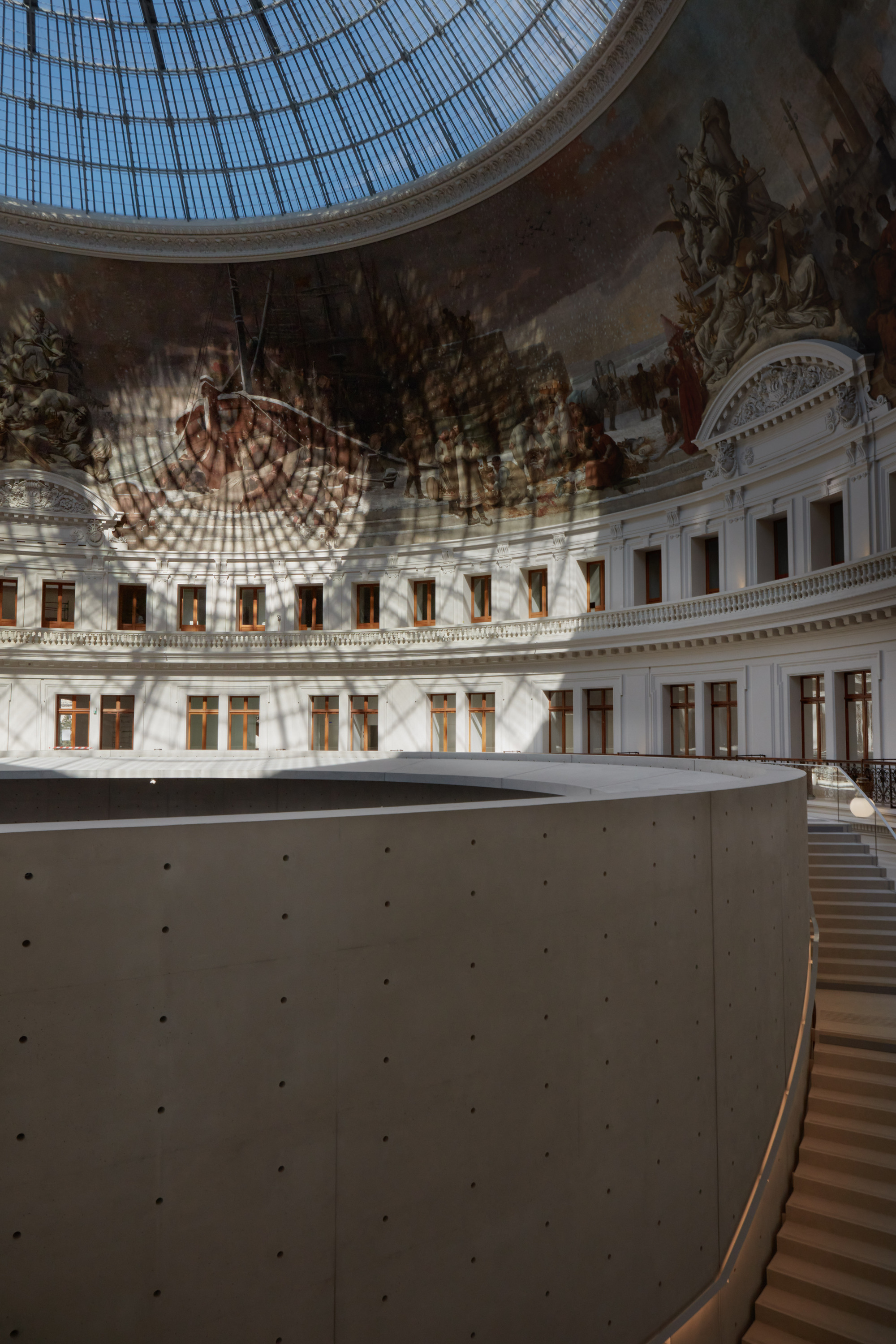 Paris' La Bourse de Commerce redesigned by Tadao Ando — Sunlight filters through the geometric steel-framed glass cupola, casting a precise lattice pattern across the cream-rendered walls and the monolithic...