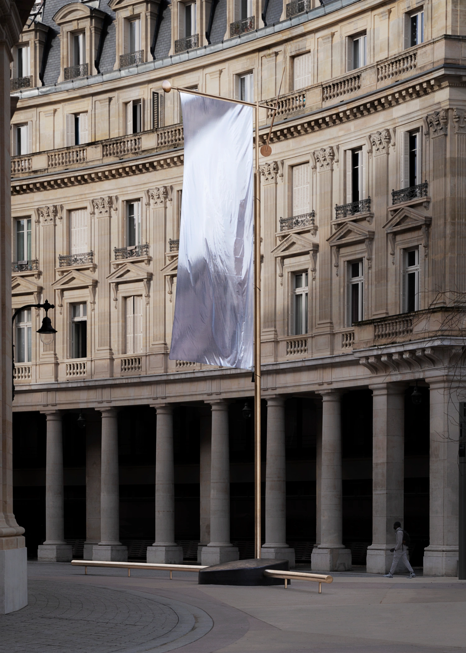 Paris' La Bourse de Commerce redesigned by Tadao Ando — A suspended fabric banner hangs vertically between the colonnaded arcade and the perforated concrete cylinder, its white surface marked by gestural grey...