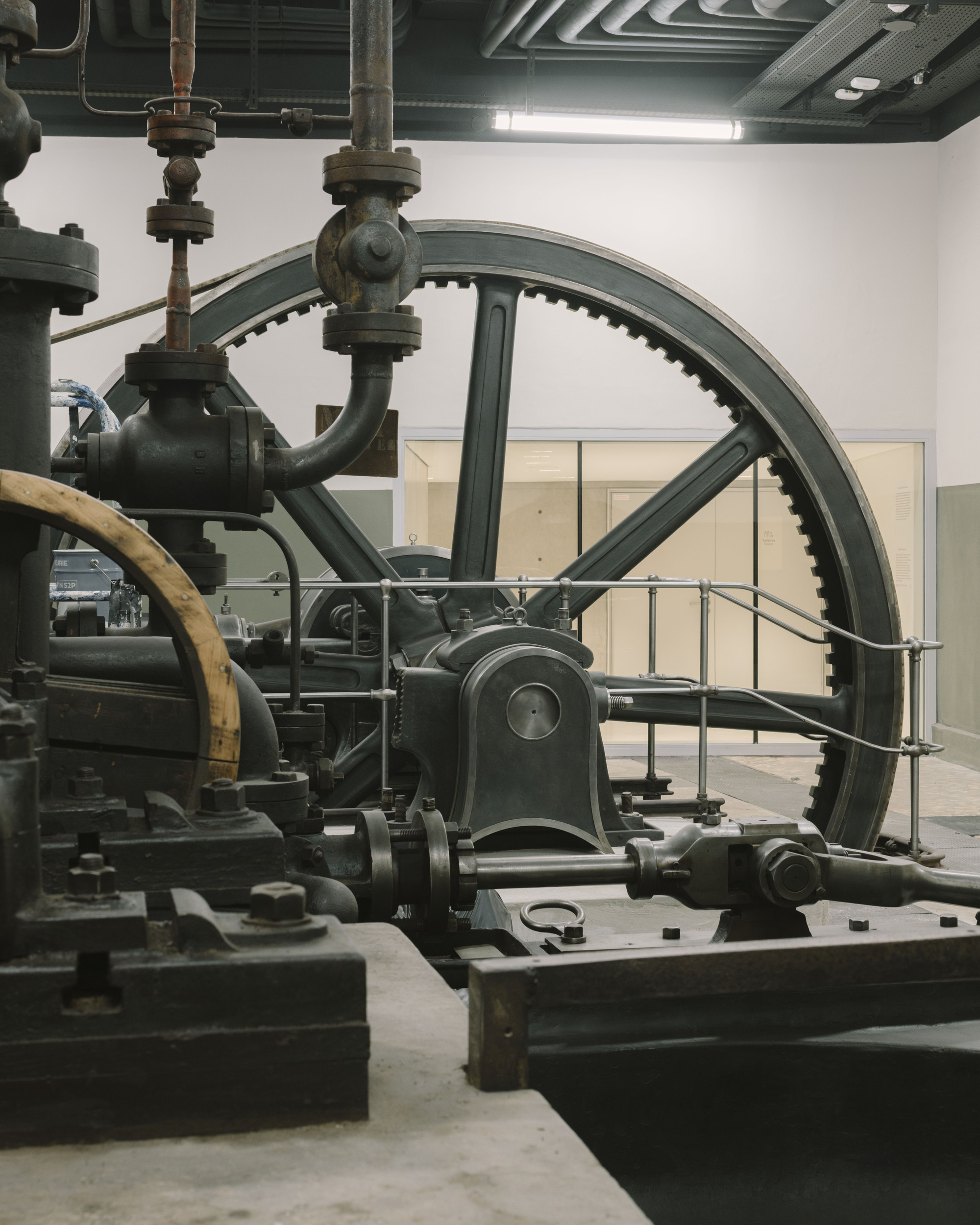Paris' La Bourse de Commerce redesigned by Tadao Ando — A close-up view of a cast-iron engine mechanism, featuring a massive gear wheel with precisely-machined teeth and a central spherical bearing assembly.