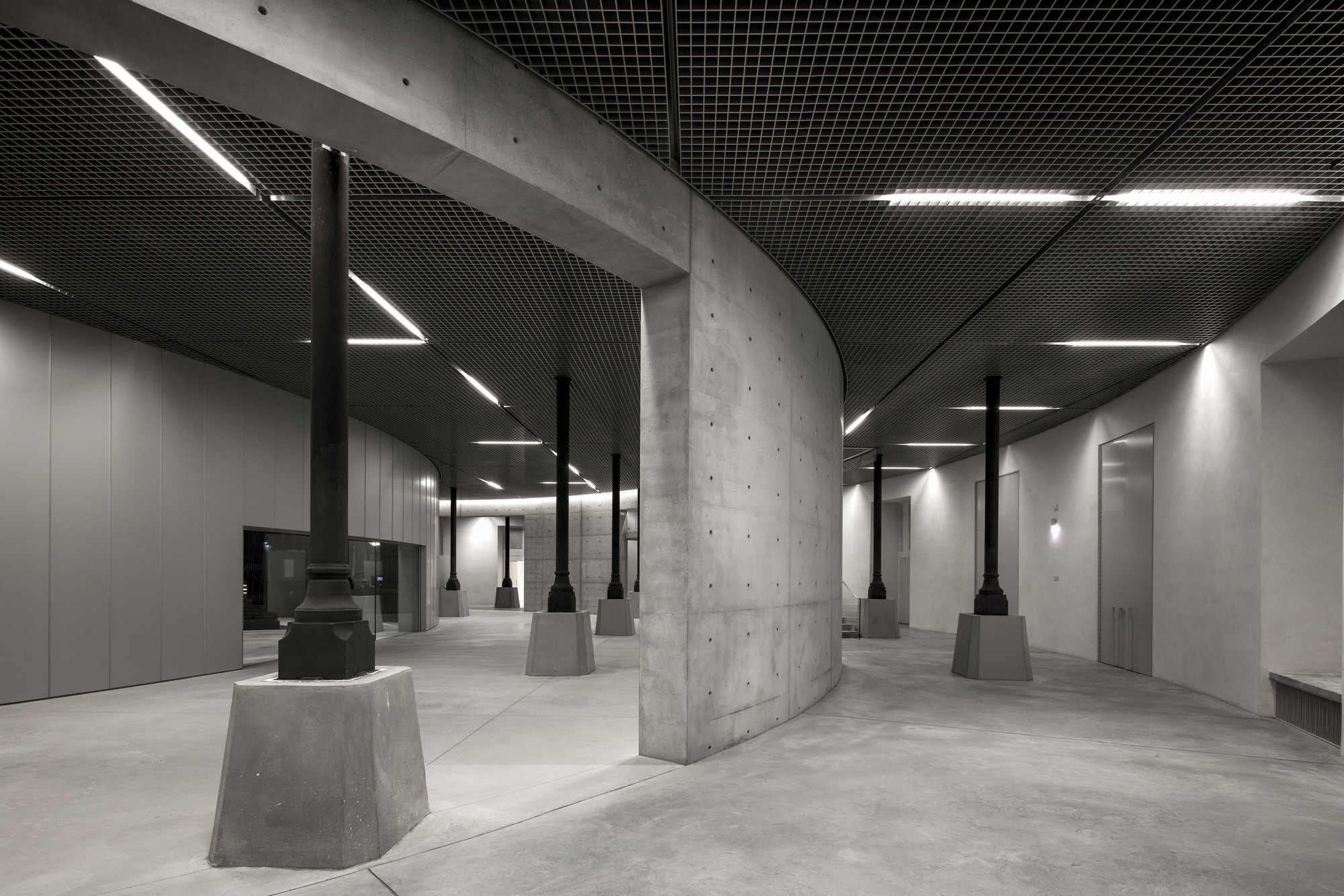 Paris' La Bourse de Commerce redesigned by Tadao Ando — The interventionist concrete cylinder dominates the foreground of this subterranean gallery space, its monolithic form anchored by trapezoidal concrete...