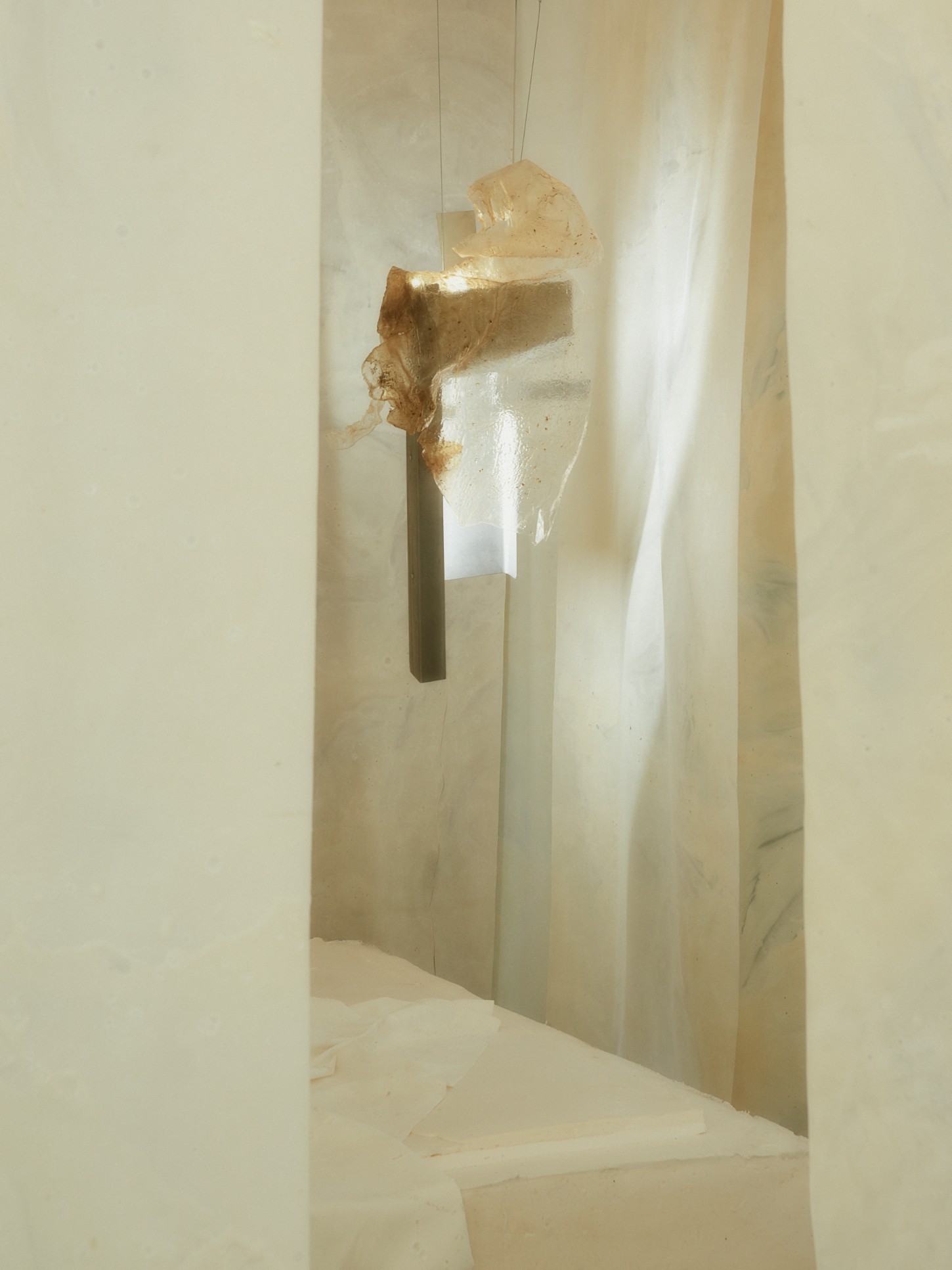 'White Utopia' by Natural Material Studio — A suspended sculptural head in patinated brass or bronze occupies a narrow vertical alcove carved into cream-colored walls.