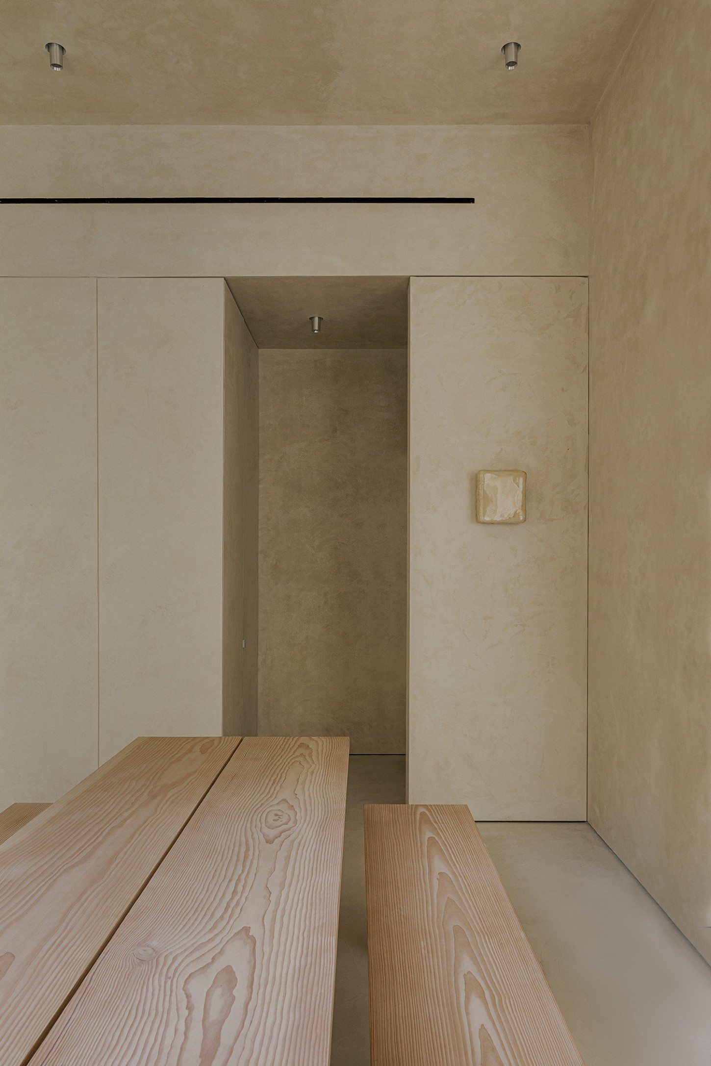ZØ Residence by Studio Beta Ø — A minimalist passage featuring a monolithic timber table and raw wooden benches in the foreground, their grain patterns rendered in sharp detail.