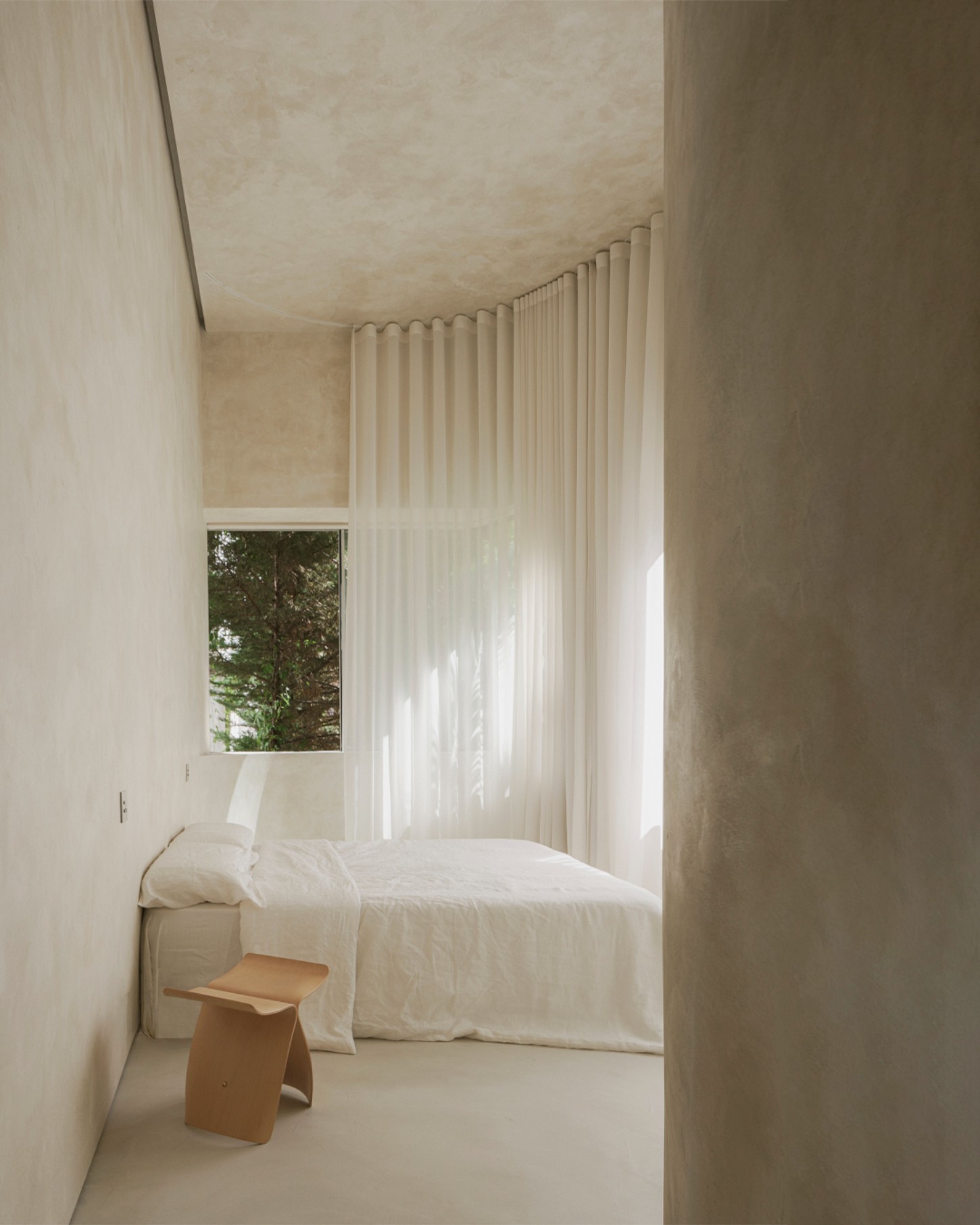 ZØ Residence by Studio Beta Ø — A narrow bedroom alcove with floor-to-ceiling vertical ribbed fabric curtains filtering daylight across cream-rendered walls.