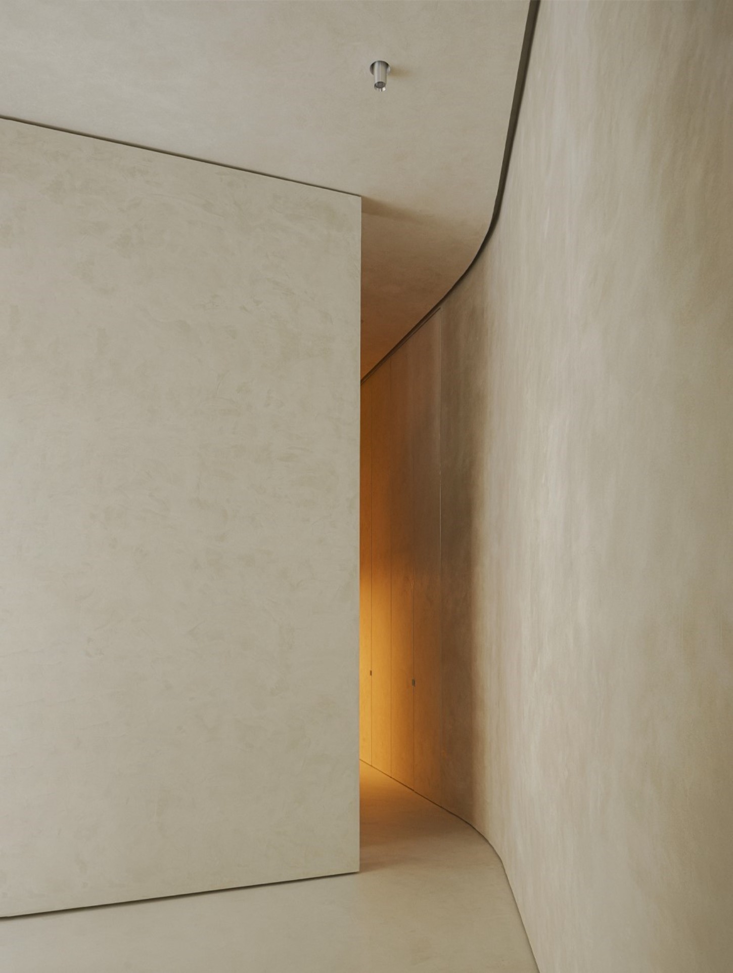 ZØ Residence by Studio Beta Ø — A narrow passage frames a threshold between two material zones: cream-colored plaster walls converge toward a wooden interior visible through the opening,...