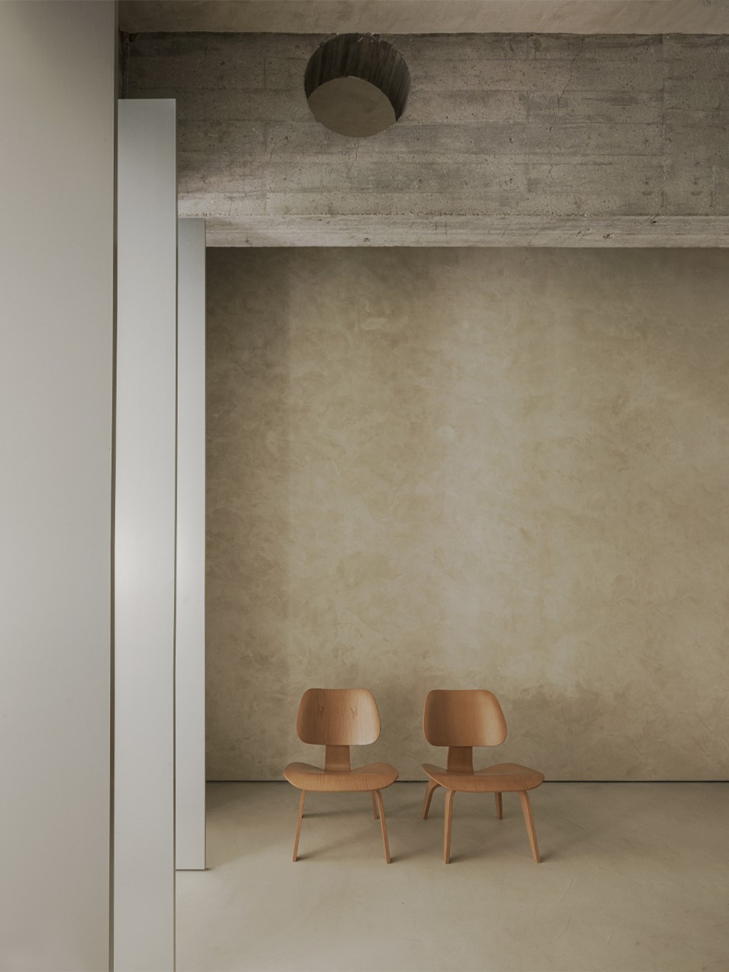 ZØ Residence by Studio Beta Ø — A recessed alcove frames two sculptural wooden chairs with organic curved backs and tapered legs, positioned against a rendered concrete wall.