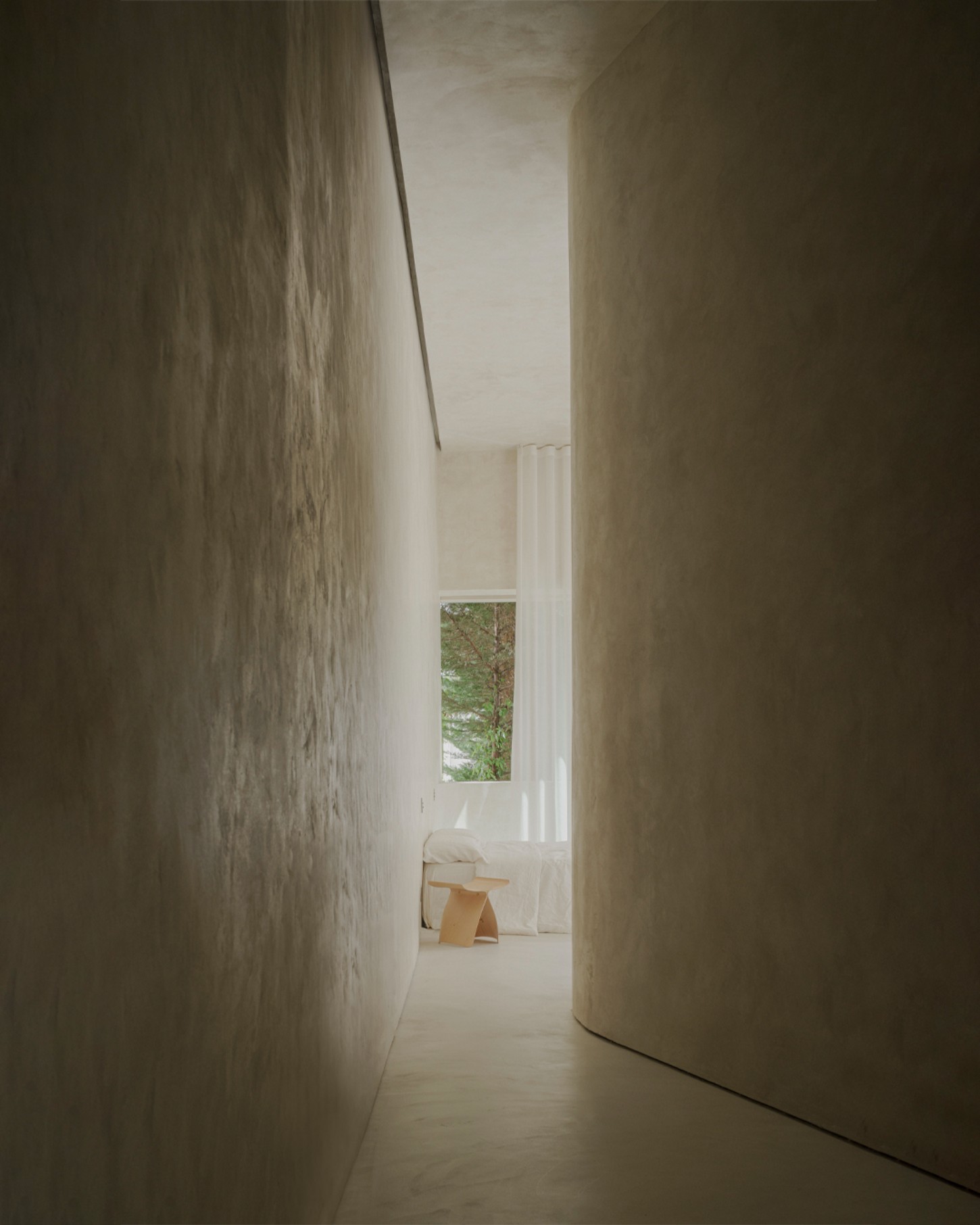 ZØ Residence by Studio Beta Ø — A narrow passage frames the minimal interior through two monolithic concrete walls, their ribbed surface texture catching lateral light.
