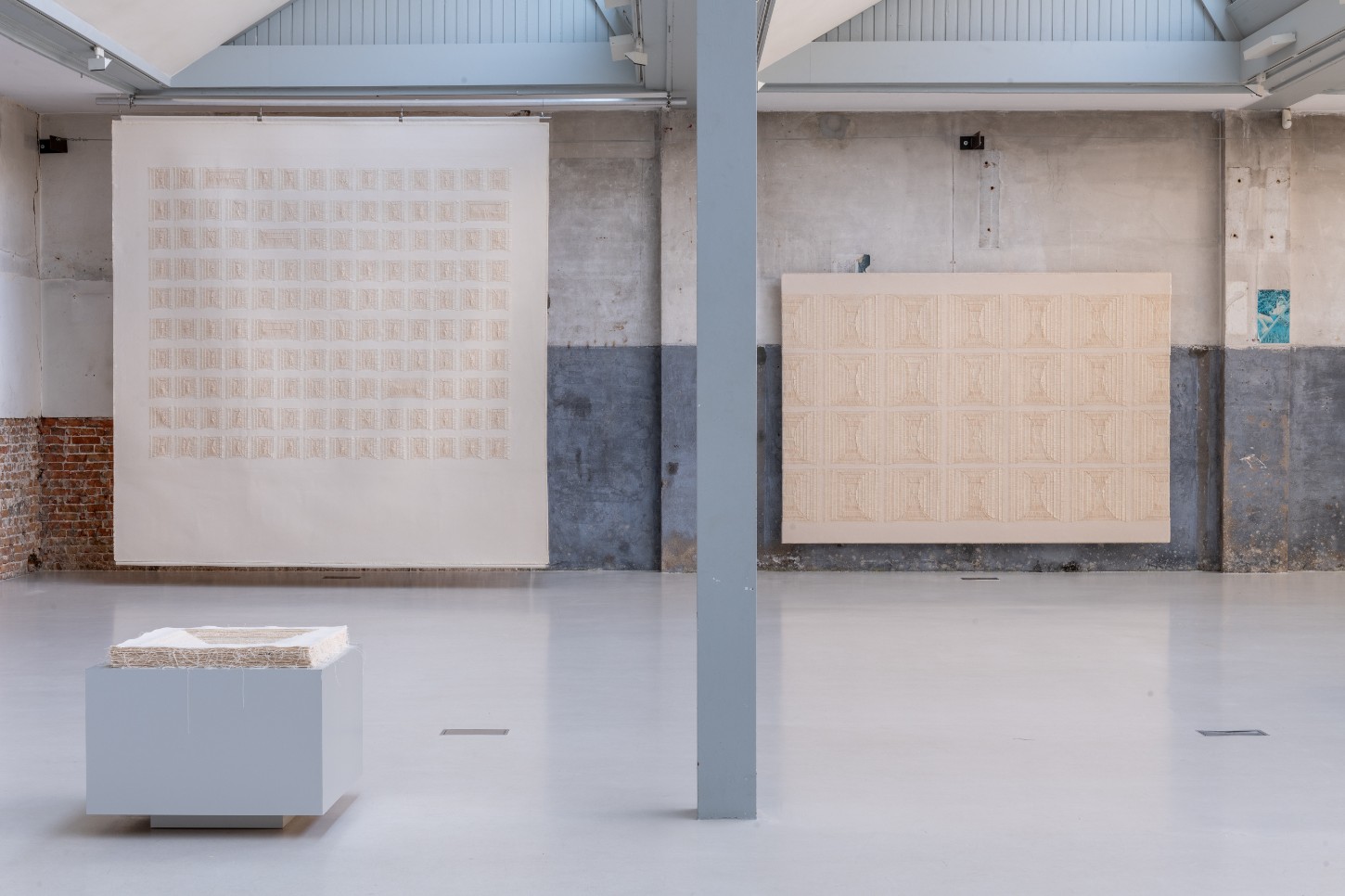 'Repetition is a Form of Change' by Sophie Rowley at Looiersgracht 60 — Sophie Rowley's wall-mounted textile work occupies the left gallery wall, presenting a grid of approximately 120 hand-woven rectangular units arranged in 12...
