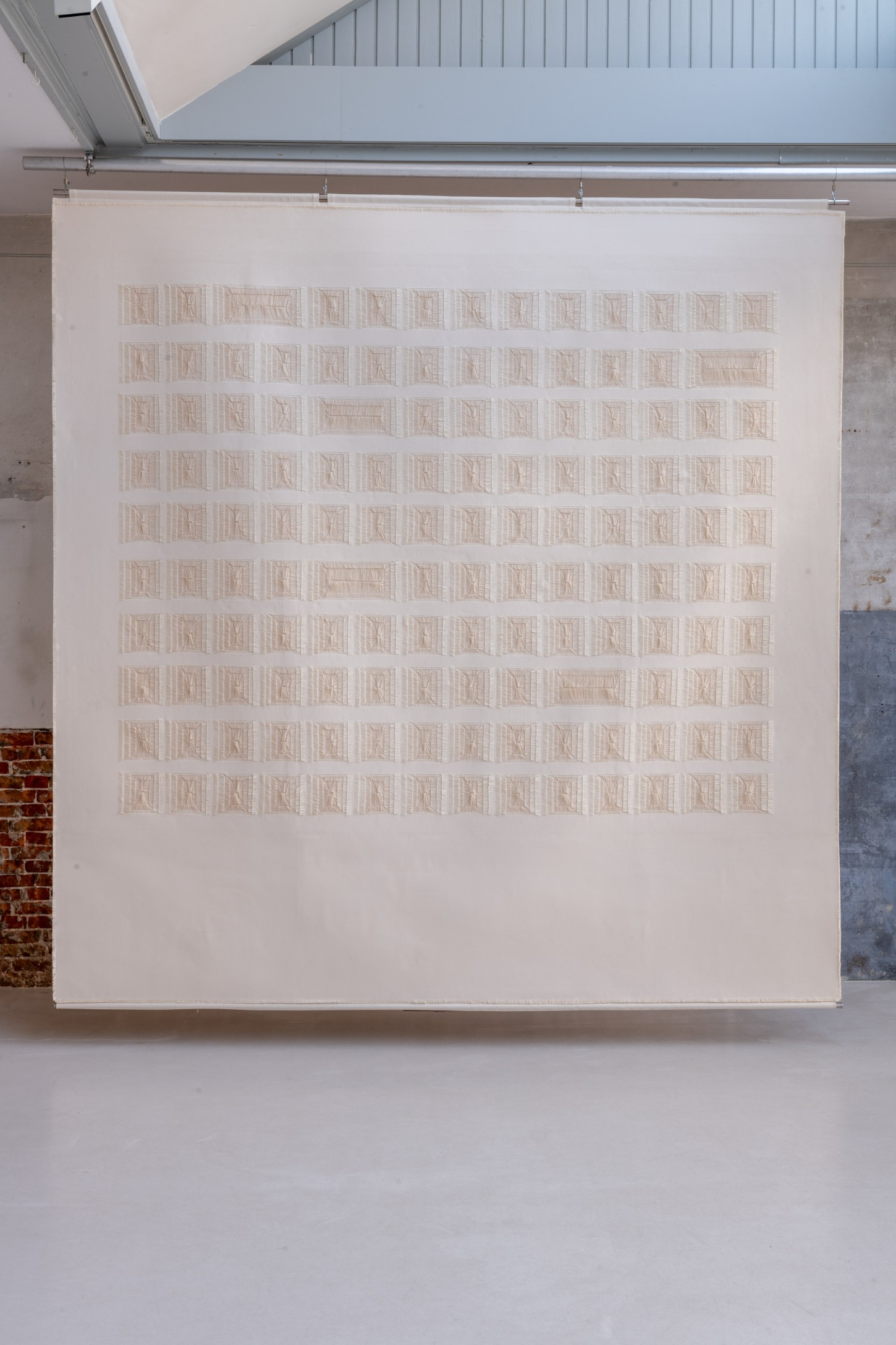 'Repetition is a Form of Change' by Sophie Rowley at Looiersgracht 60 — A large-scale woven work suspended in a gallery space comprises approximately 120 individual rectangular textile units arranged in a 12-row grid.