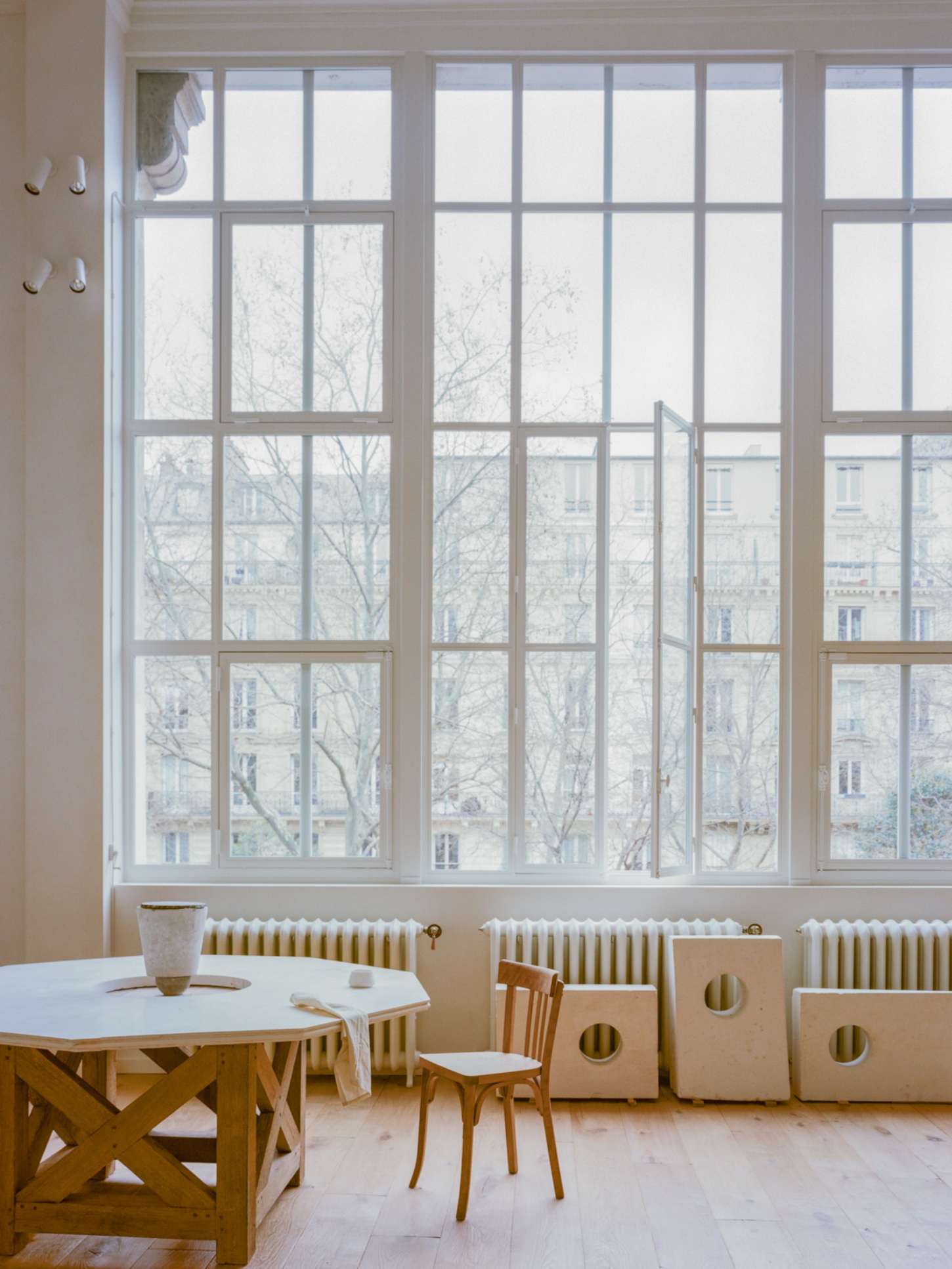 Casey Casey Showroom by Atelier NEA — A Paris showroom bathed in diffused northern light through expansive steel-framed windows with a 16-pane grid pattern.