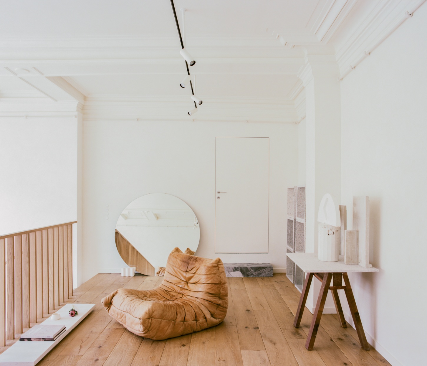 Casey Casey Showroom by Atelier NEA — The showroom's central volume features a cognac leather sculptural seating element positioned on pale pine floorboards, accompanied by a circular mirror...