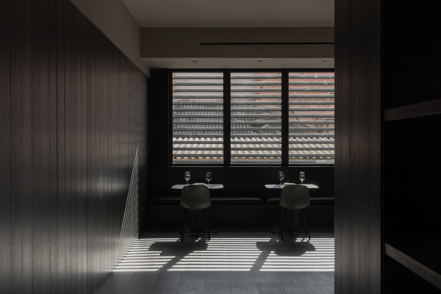 Tritium Winery by Francesc Rifé Studio — A minimalist tasting room bathed in linear light patterns from three horizontal-slat windows overlooking vineyard rows.