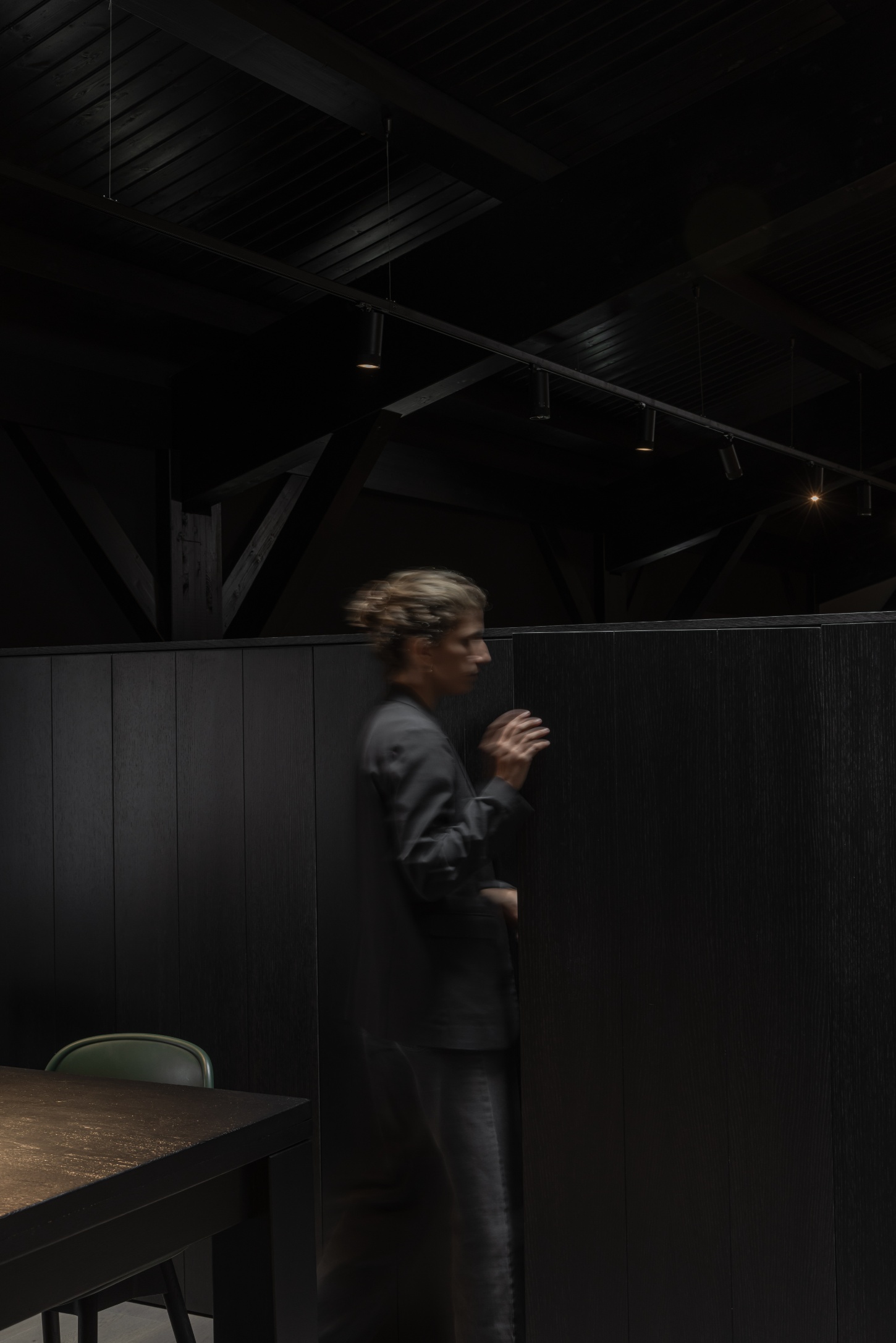 Tritium Winery by Francesc Rifé Studio — A figure in profile stands within a darkened interior, silhouetted against black timber paneling.