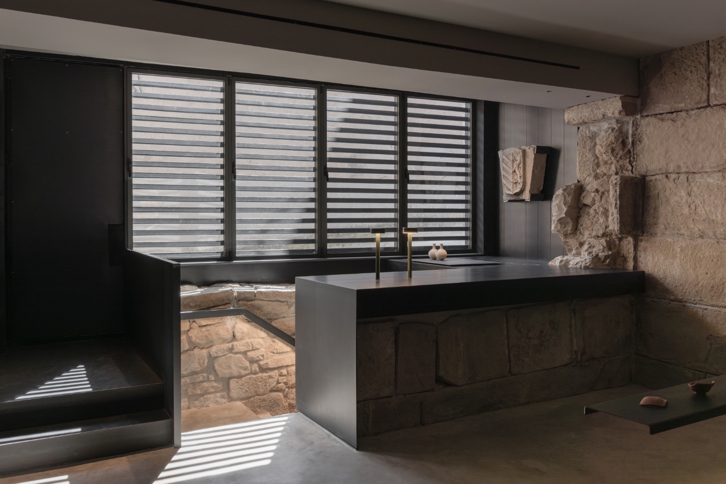 Tritium Winery by Francesc Rifé Studio — A spa or bathing space built into a 15th-century stone structure, featuring a sunken pool with monolithic charcoal-colored surround.