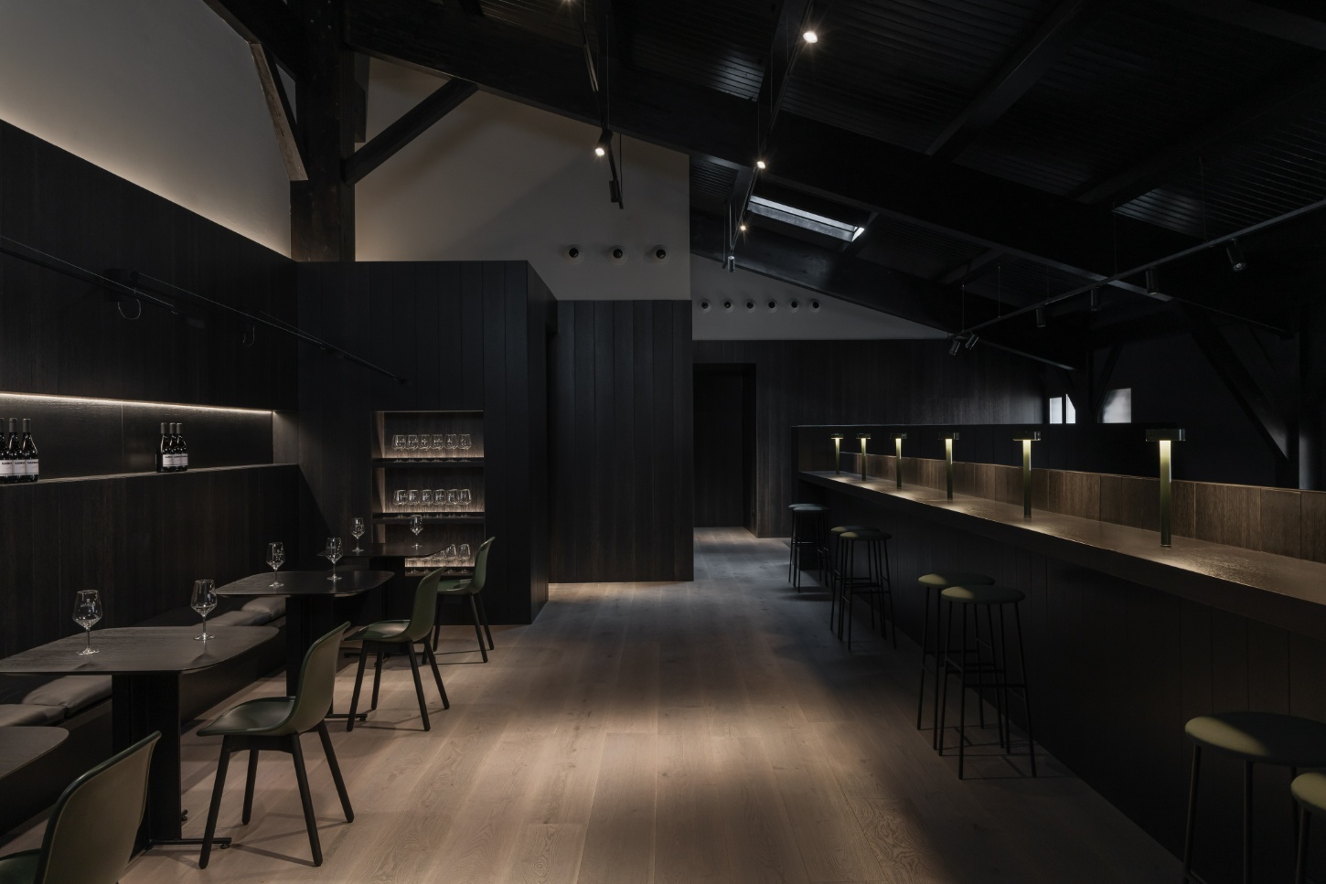 Tritium Winery by Francesc Rifé Studio — The tasting room interior showcases charred timber cladding across expansive walls, creating a monolithic dark envelope punctuated by horizontal brass-edged...